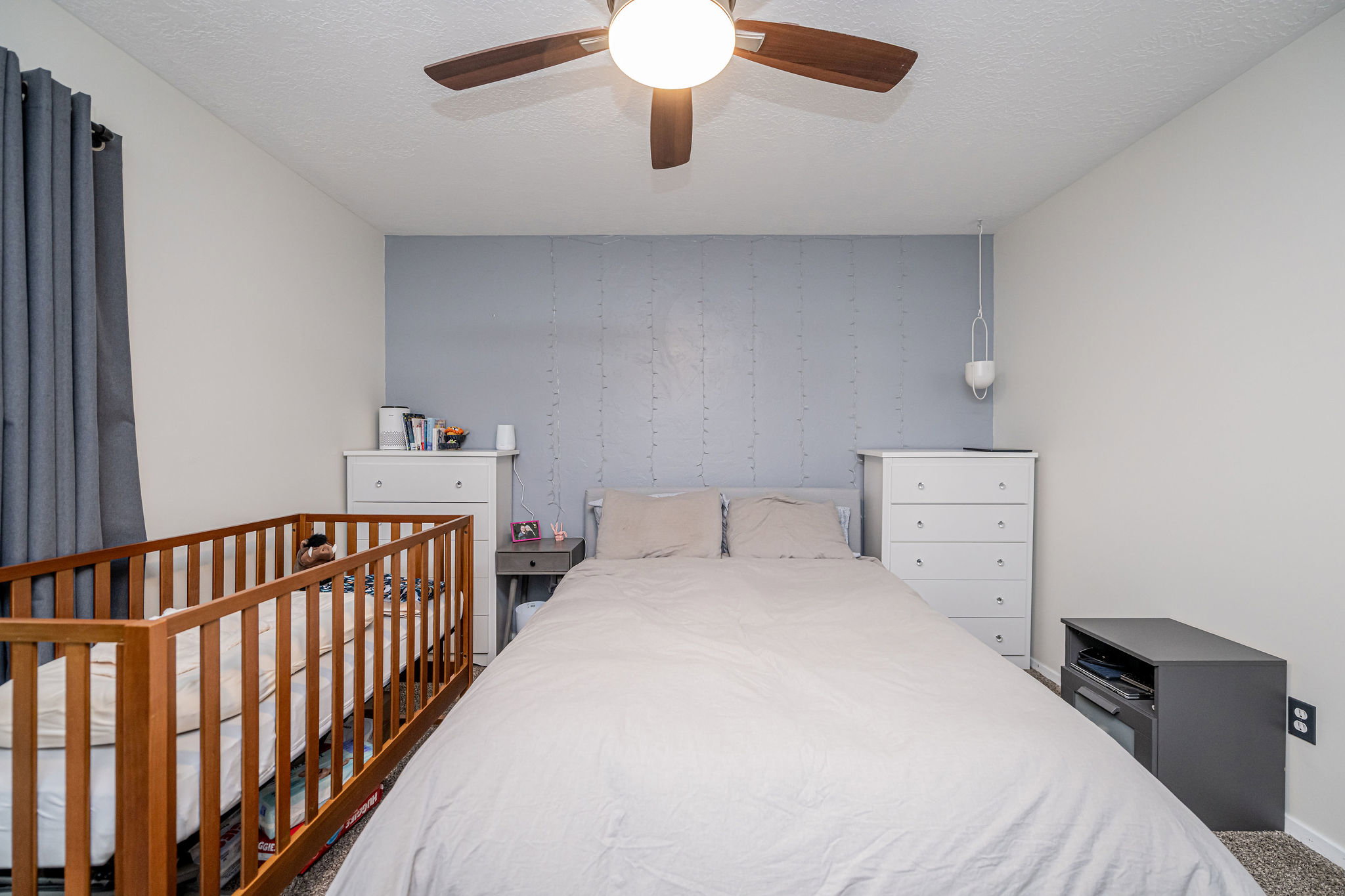 Carpeted bedroom with a ceiling fan light fixture, light gray walls, and a textured accent wall