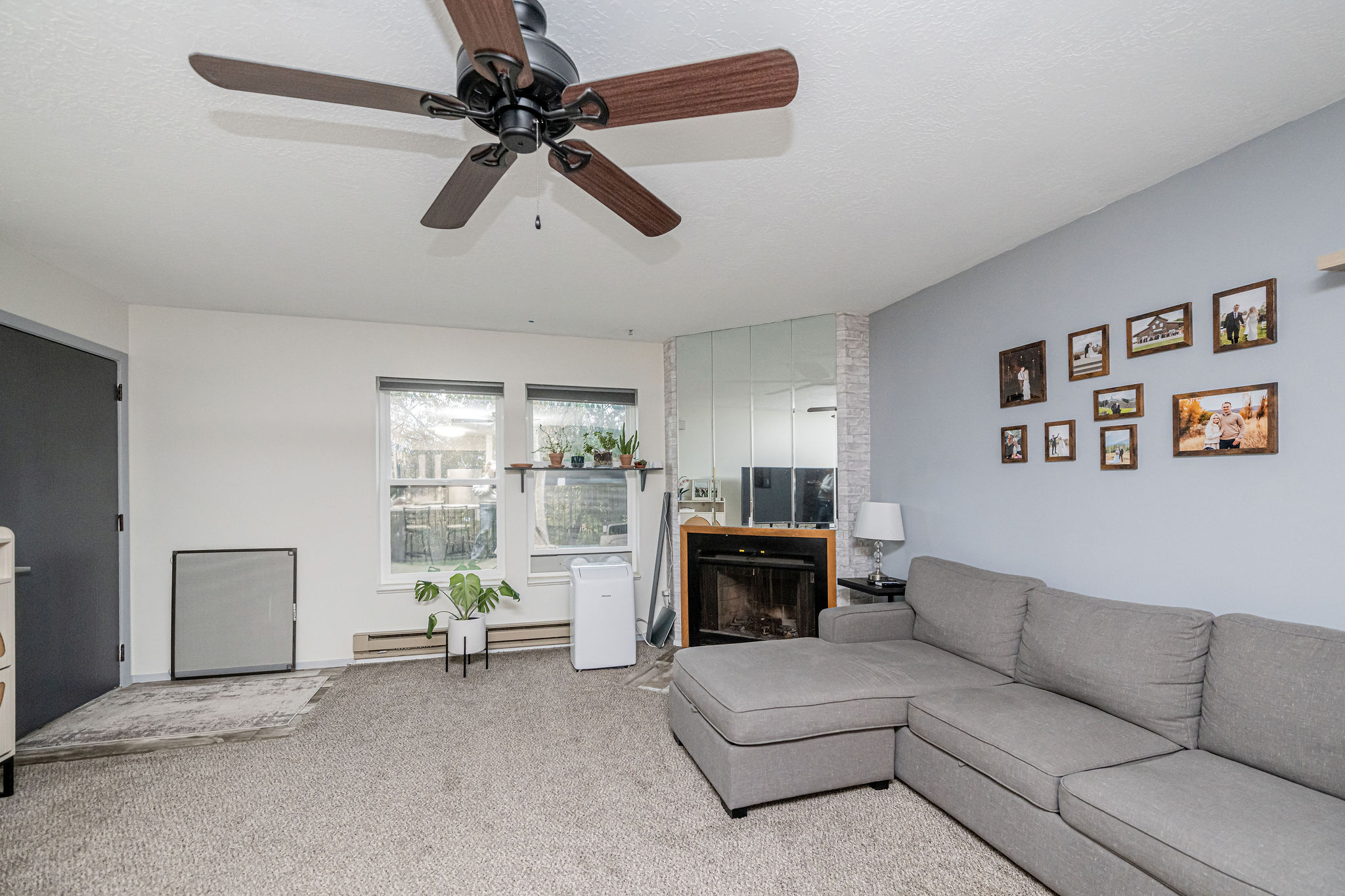 Living area with a ceiling fan, two windows, and a fireplace with mirror surround