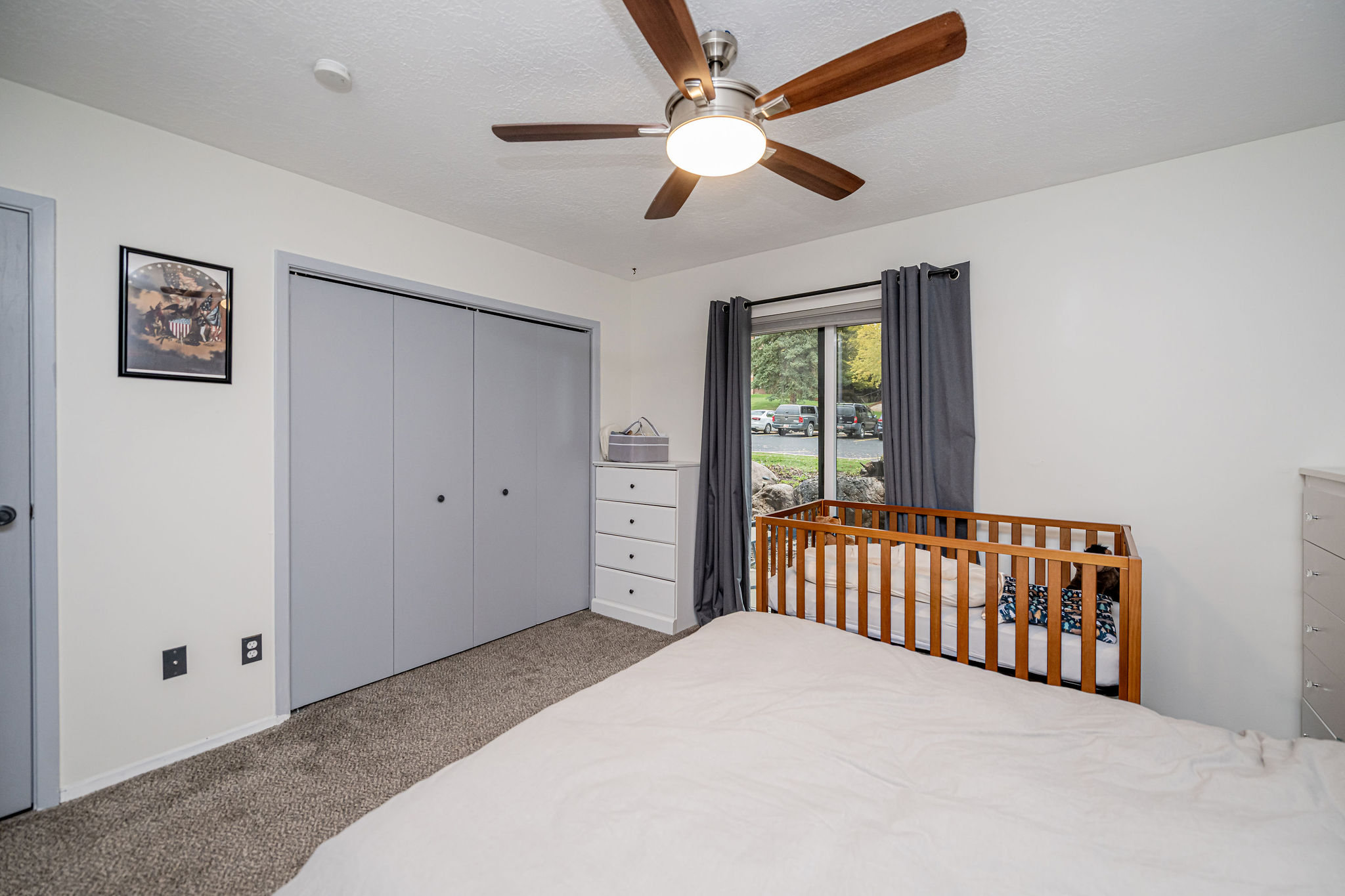Carpeted room featuring a ceiling fan with integrated lighting, a window with dark curtain panels, and bi-fold closet doors