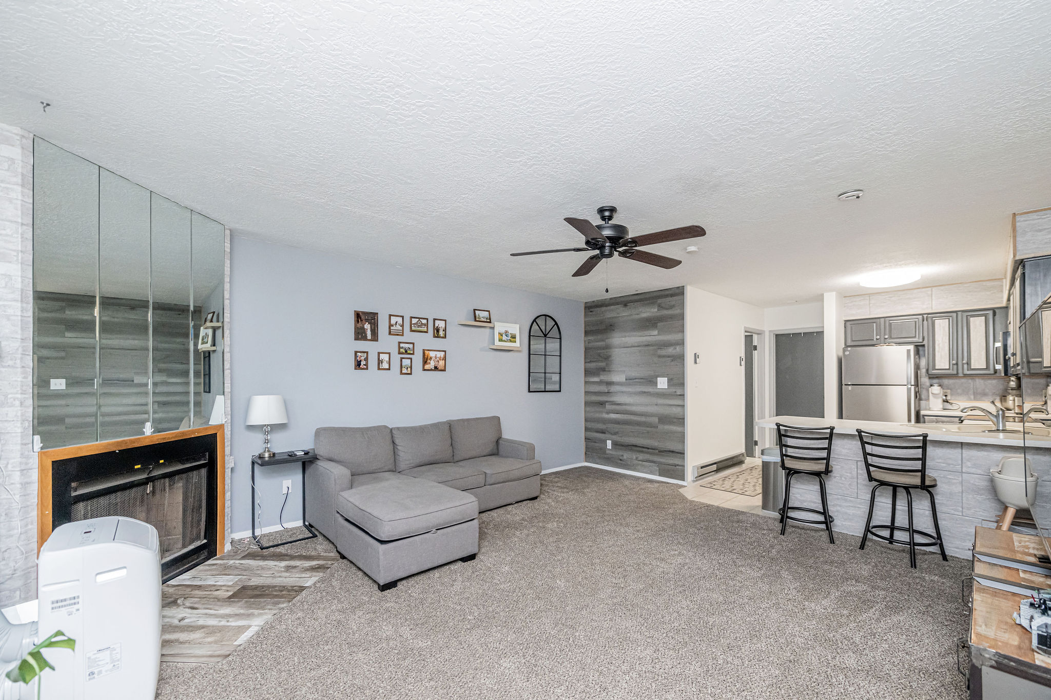 Open-concept living area featuring a fireplace with mirrored surround, textured accent wall, and a ceiling fan