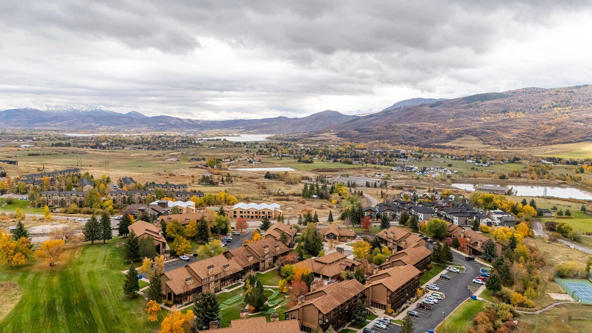 Expansive property with multiple buildings featuring pitched roofs and varied architectural styles, surrounded by mature trees with autumnal foliage