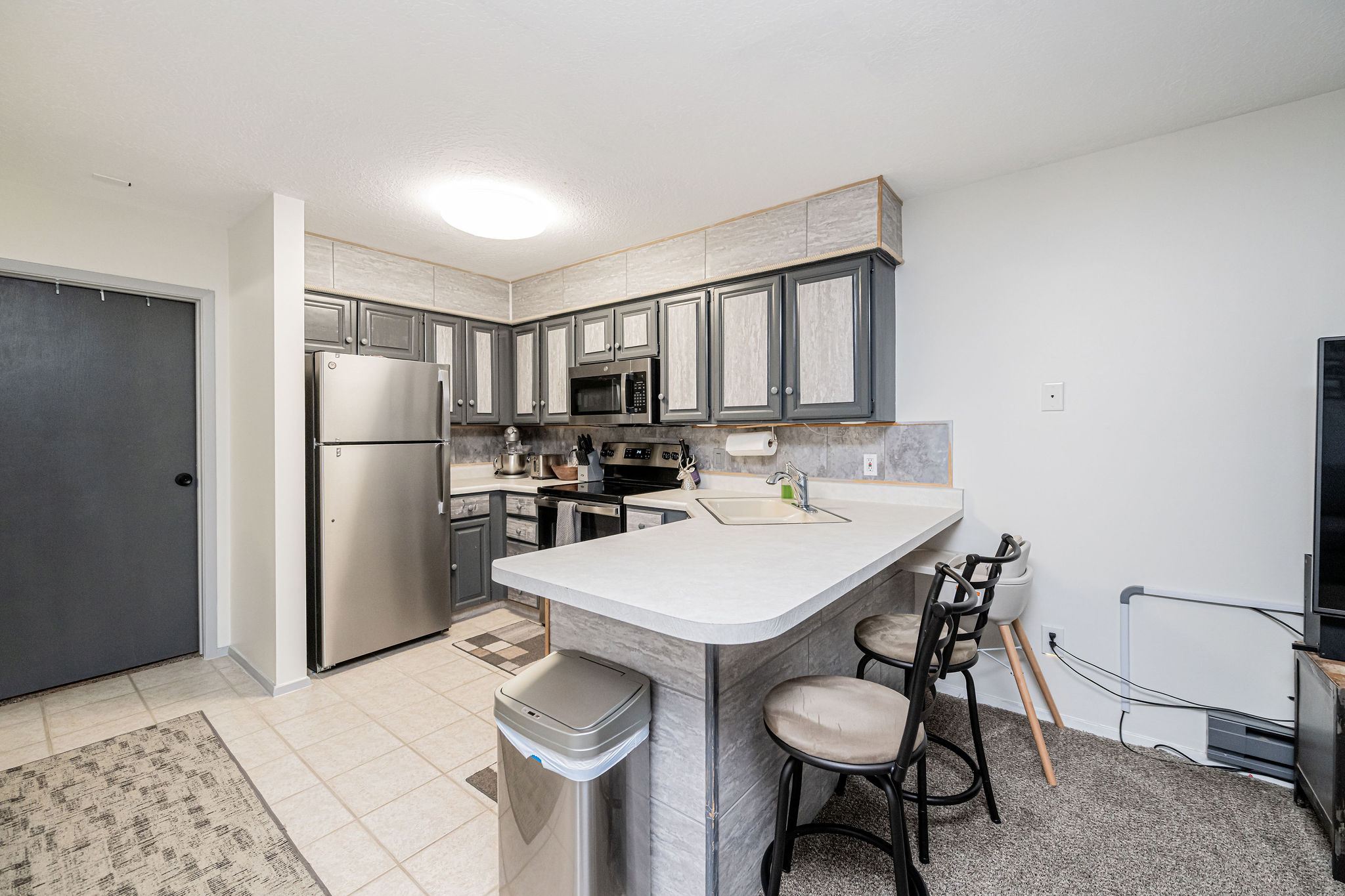 Kitchen featuring gray cabinetry with light panel inserts, stainless steel appliances, and a breakfast bar with seating