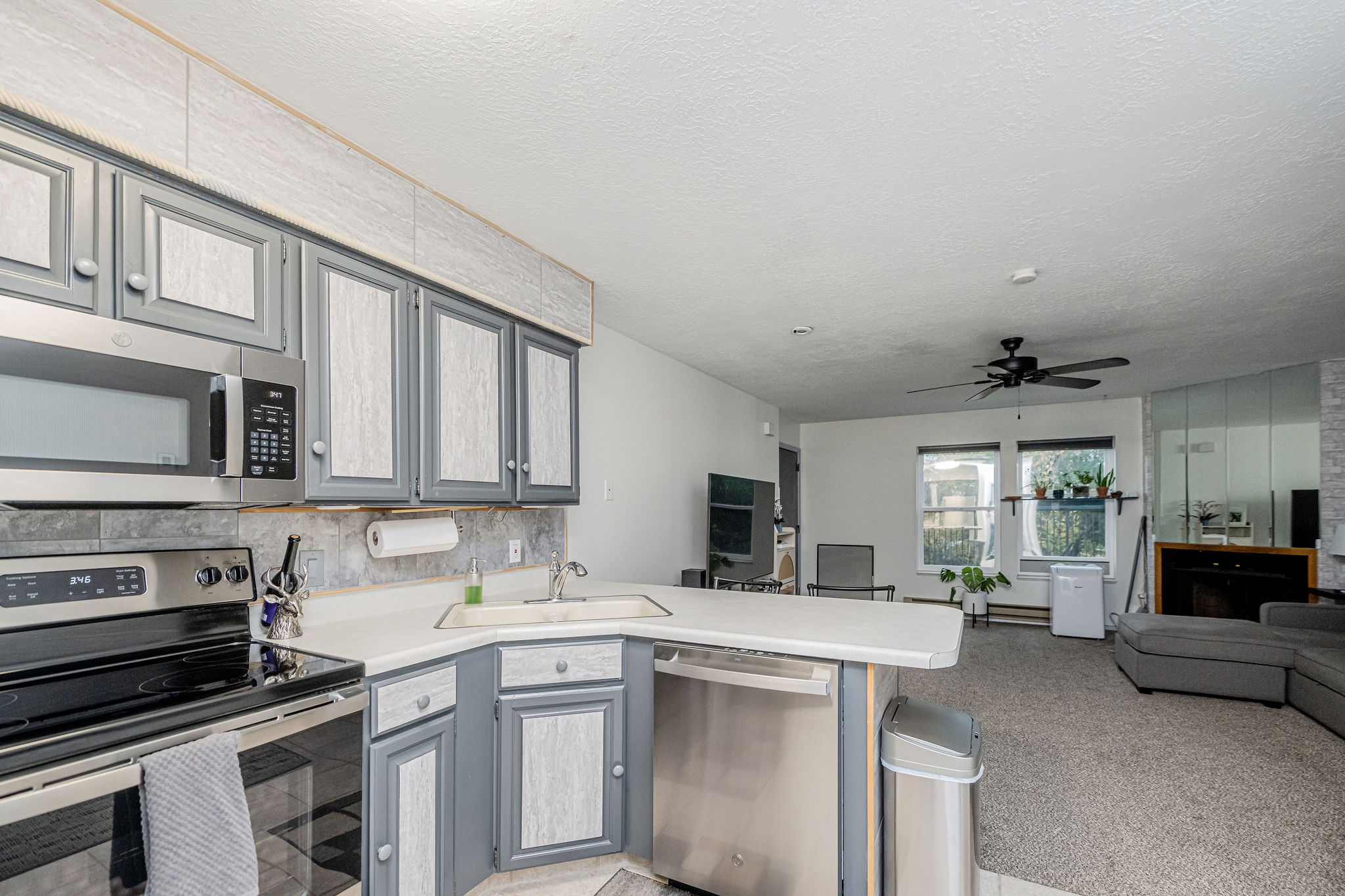 Kitchen featuring stainless steel appliances, corner sink, and gray cabinetry with light-colored inserts