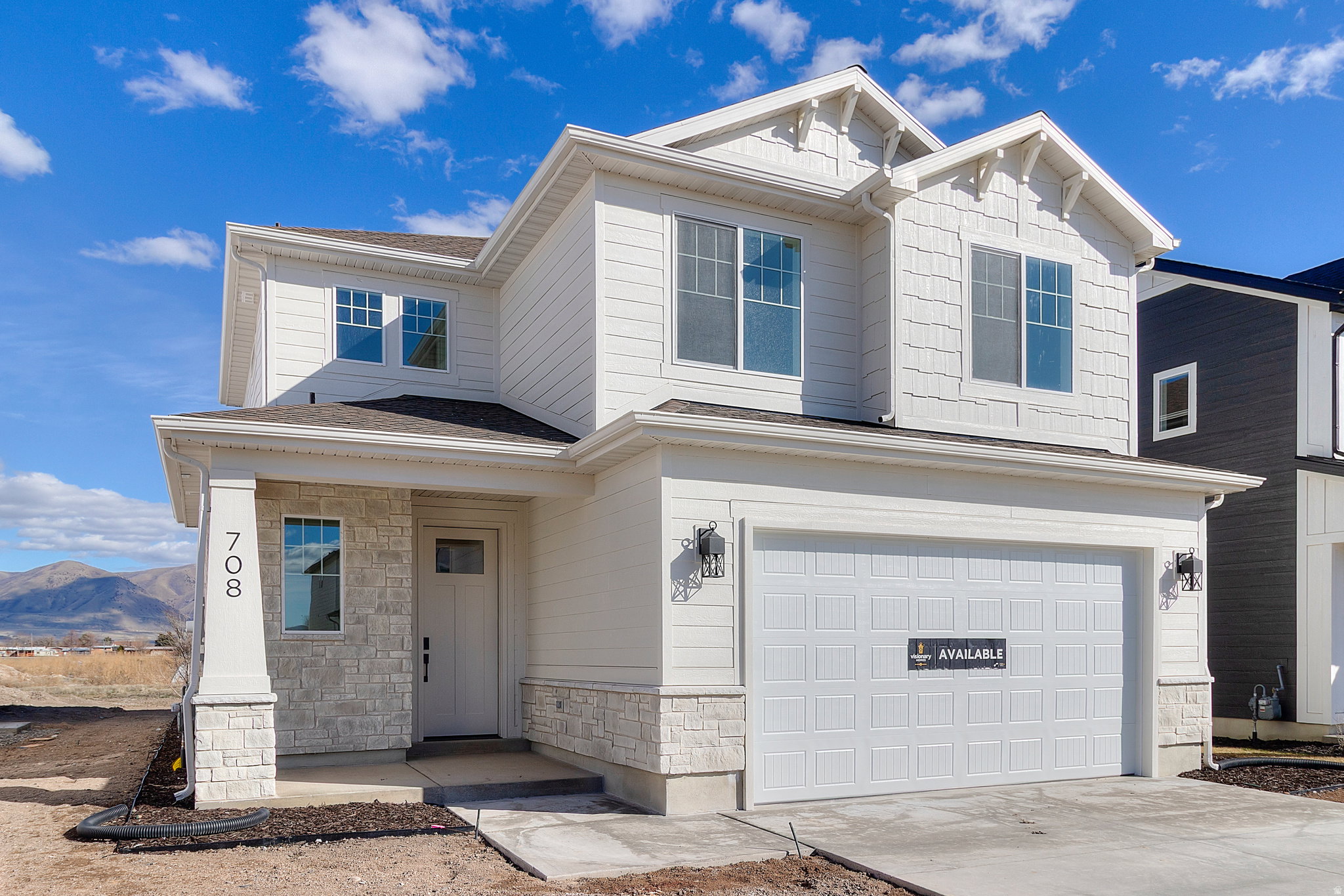 Modern two-story residence featuring white siding, a two-car garage, and stone accents