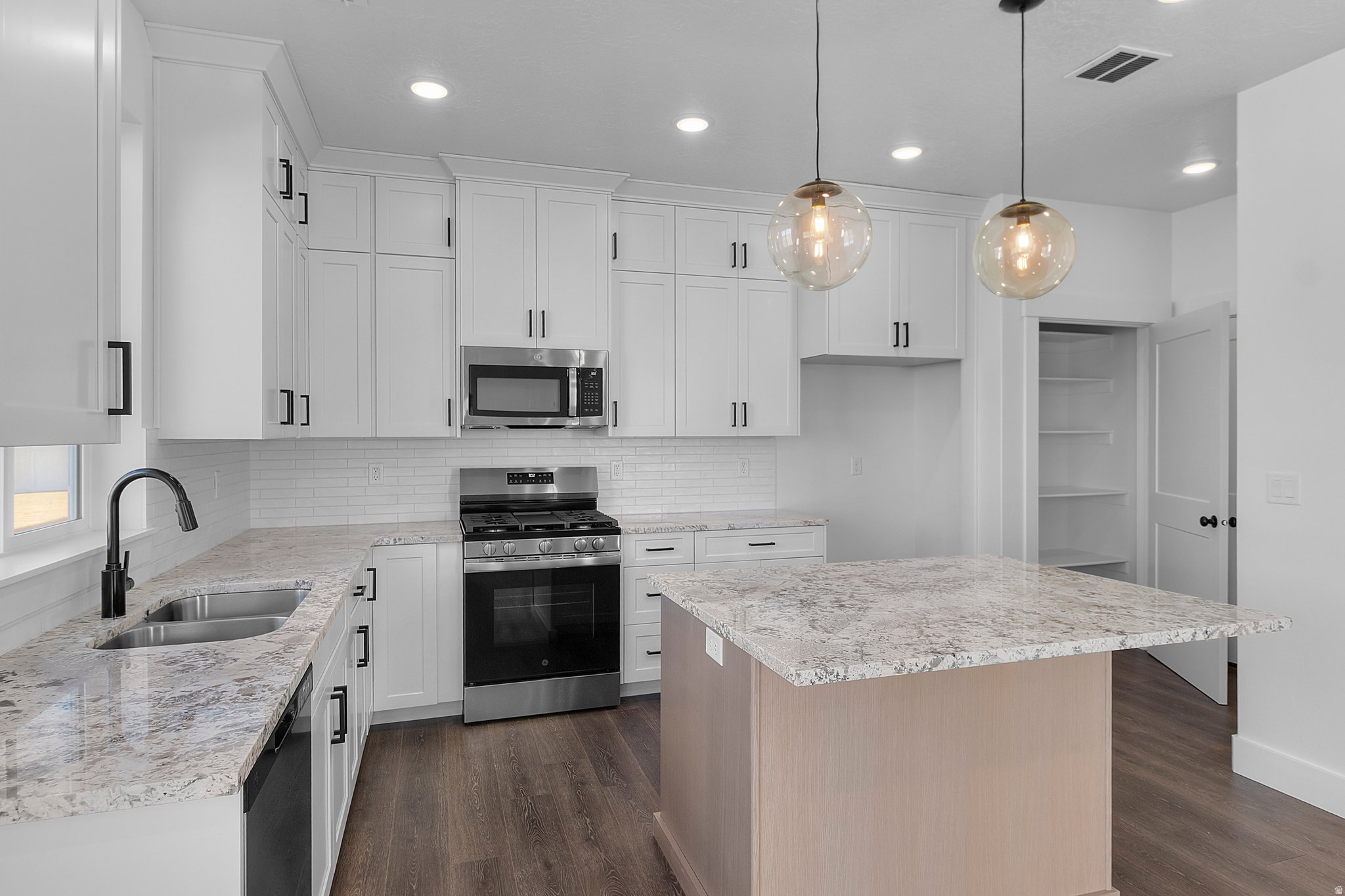 Modern kitchen featuring white shaker cabinetry with matte black hardware, stainless steel appliances, speckled countertops, and wood-finish flooring