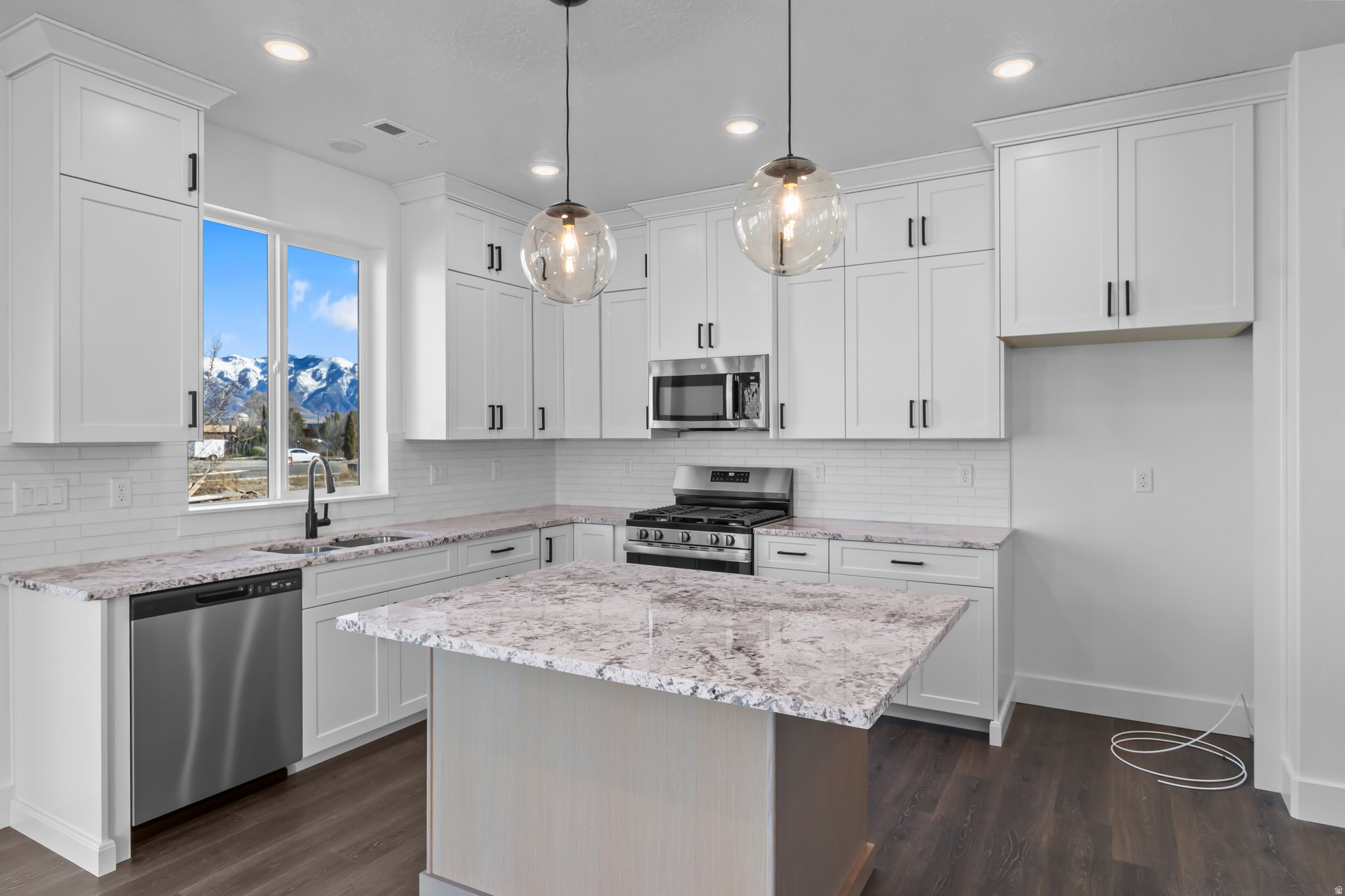 Open-concept kitchen featuring white shaker cabinetry, light-toned stone countertops, and a subway tile backsplash