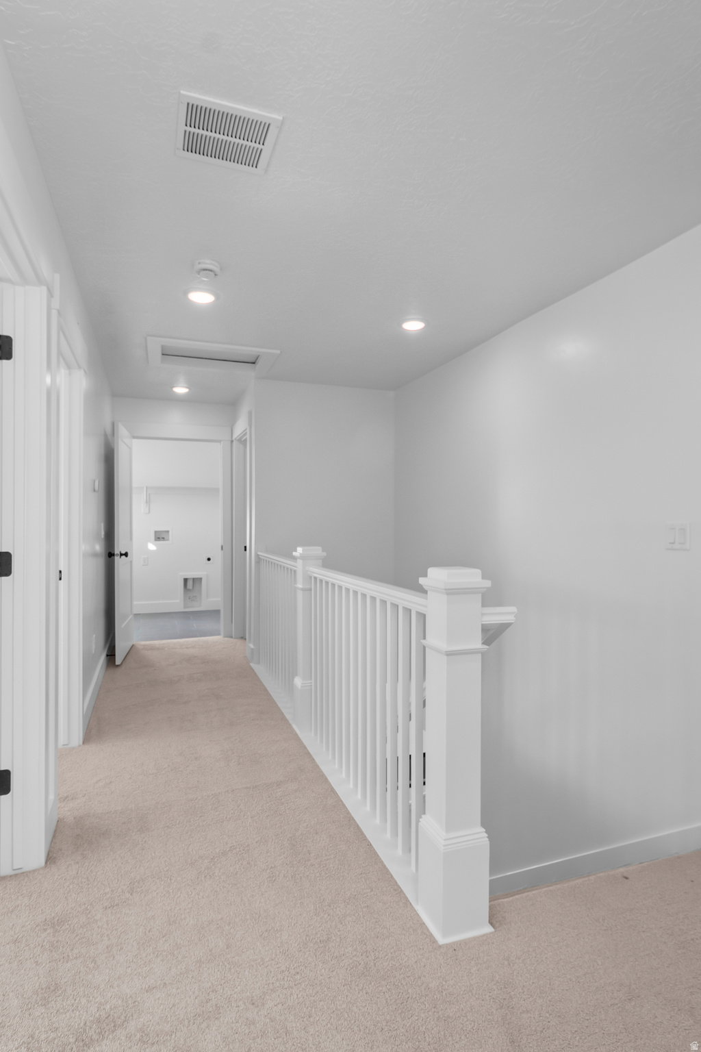 Upper-level hallway featuring neutral carpeting, recessed ceiling lighting, and a white banister with squared newel posts