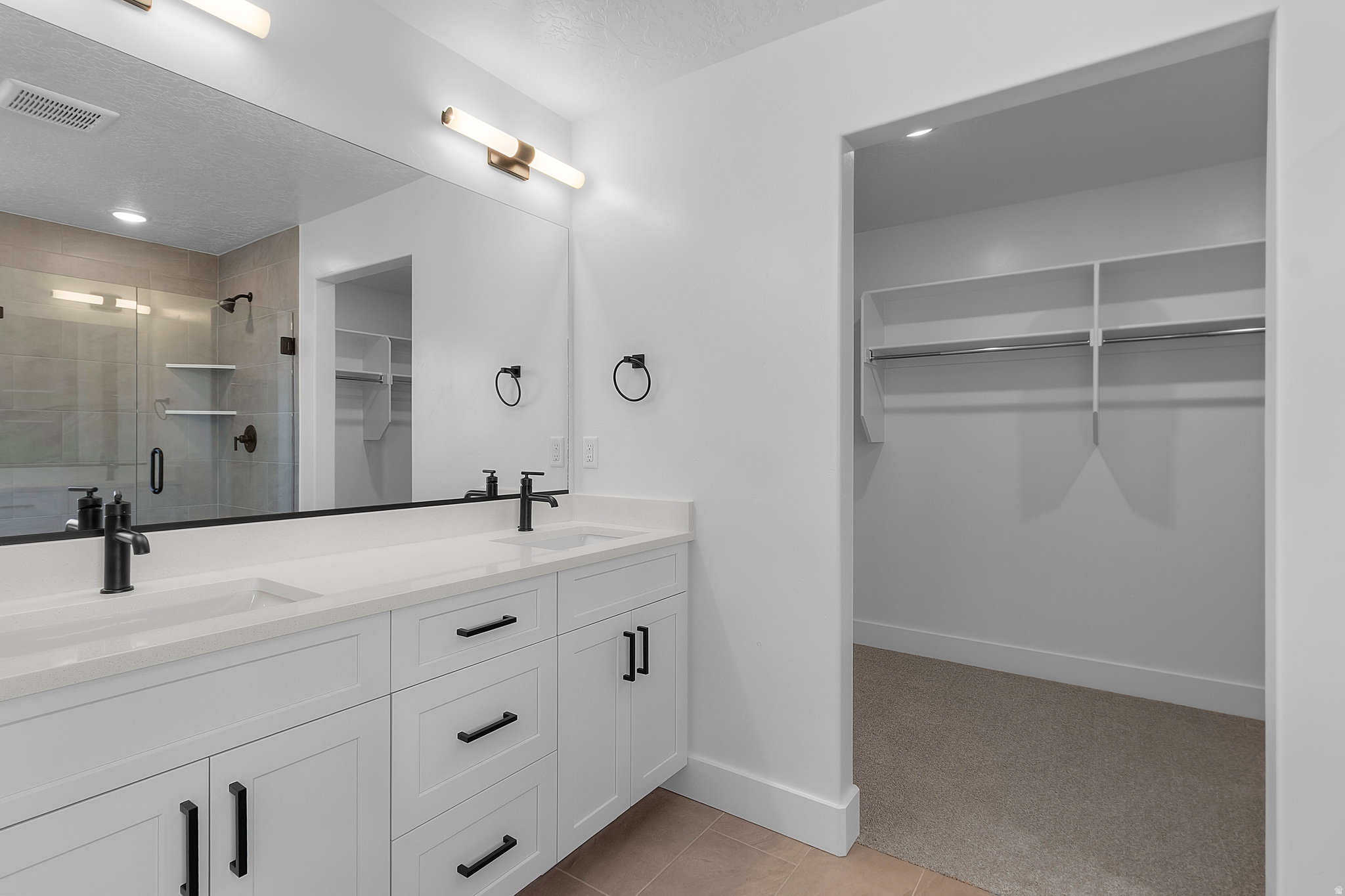 Bathroom featuring a dual vanity with white cabinetry, matte black hardware, and an expansive mirror