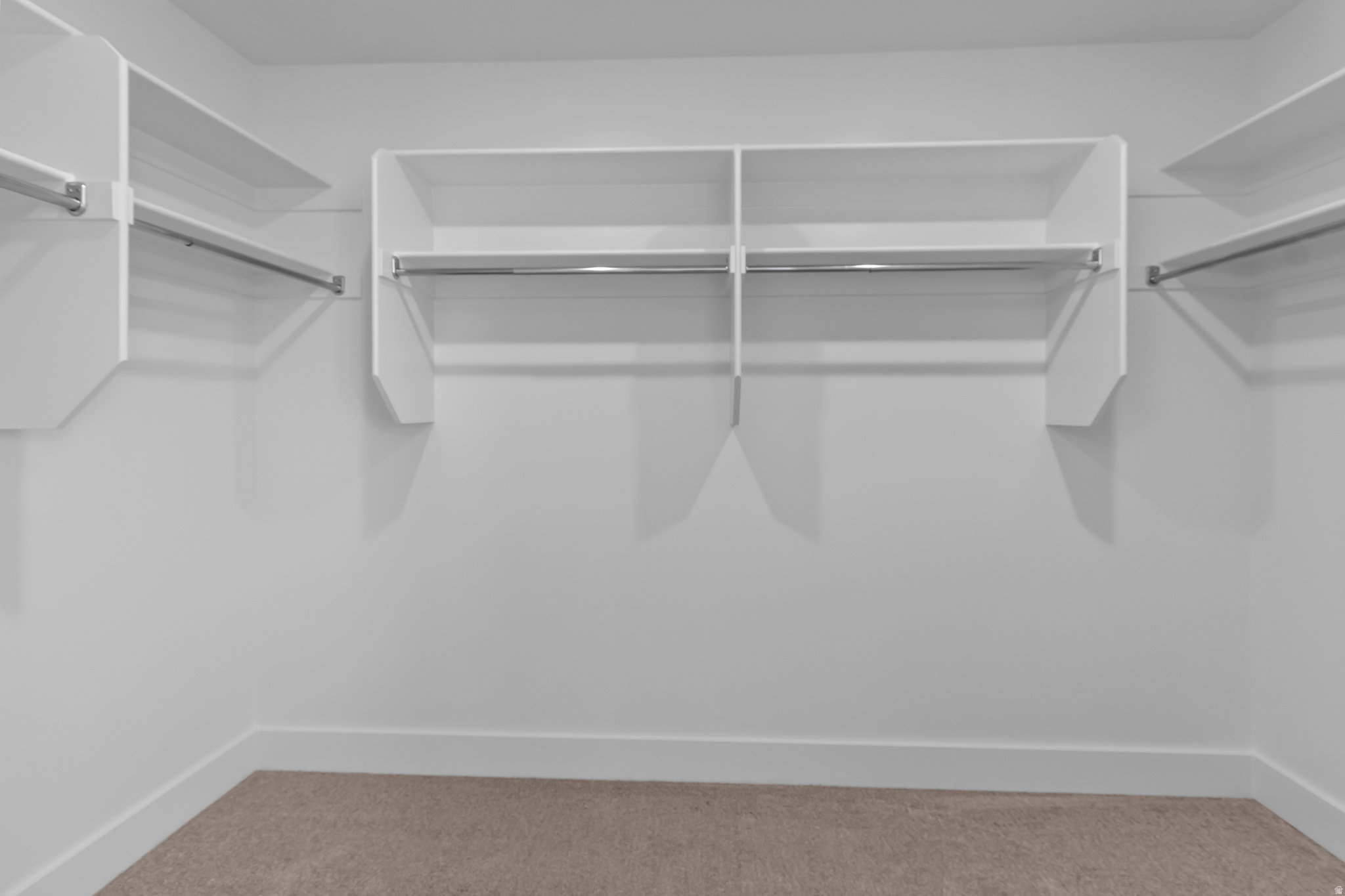 Walk-in closet with white shelving, multiple hanging rods, and neutral-toned carpeting