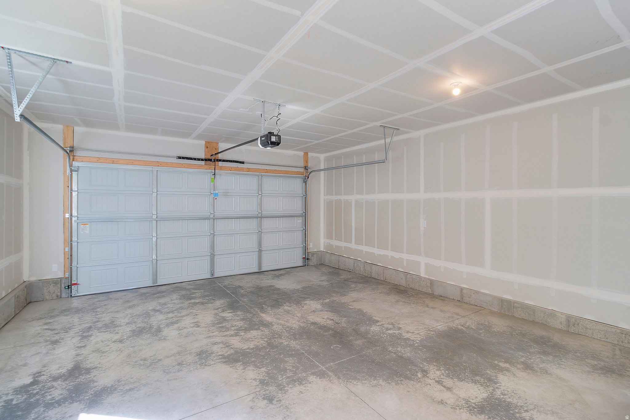 Spacious garage featuring a concrete floor, an overhead garage door, a ceiling-mounted garage door opener, and a single ceiling light fixture