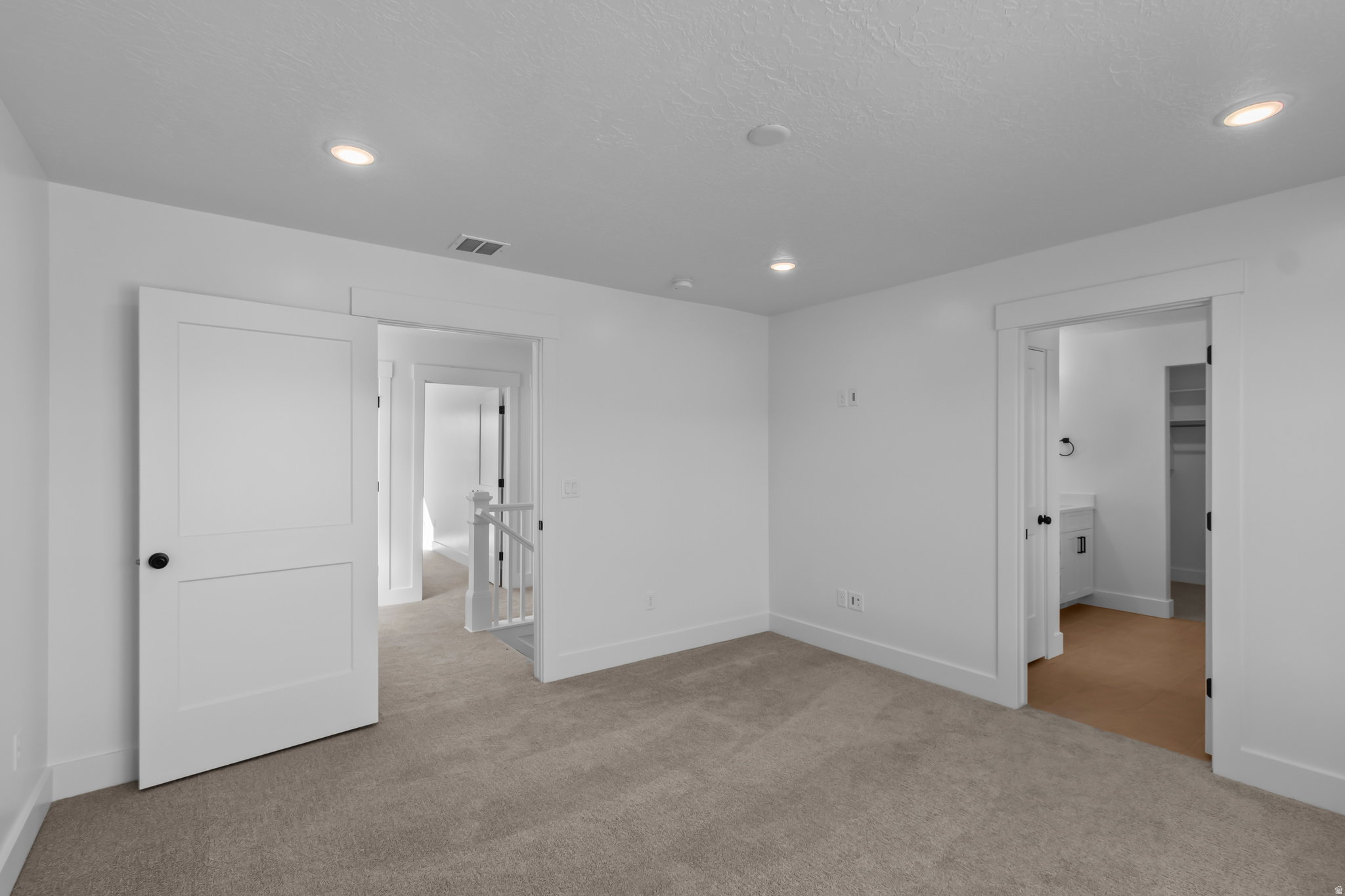 Carpeted room with recessed lighting and white trim, featuring a white paneled door with a black knob