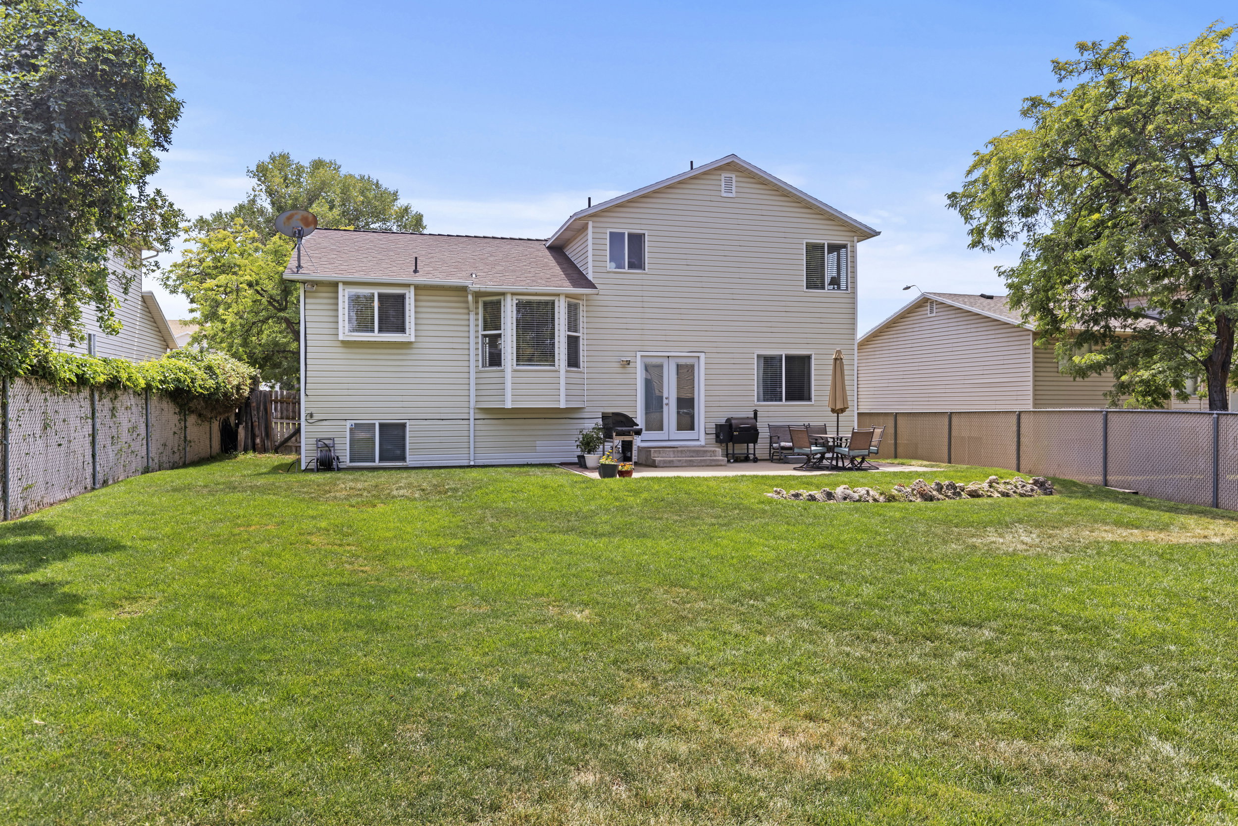 Expansive rear lawn featuring a concrete patio, light-colored siding, and a bay window