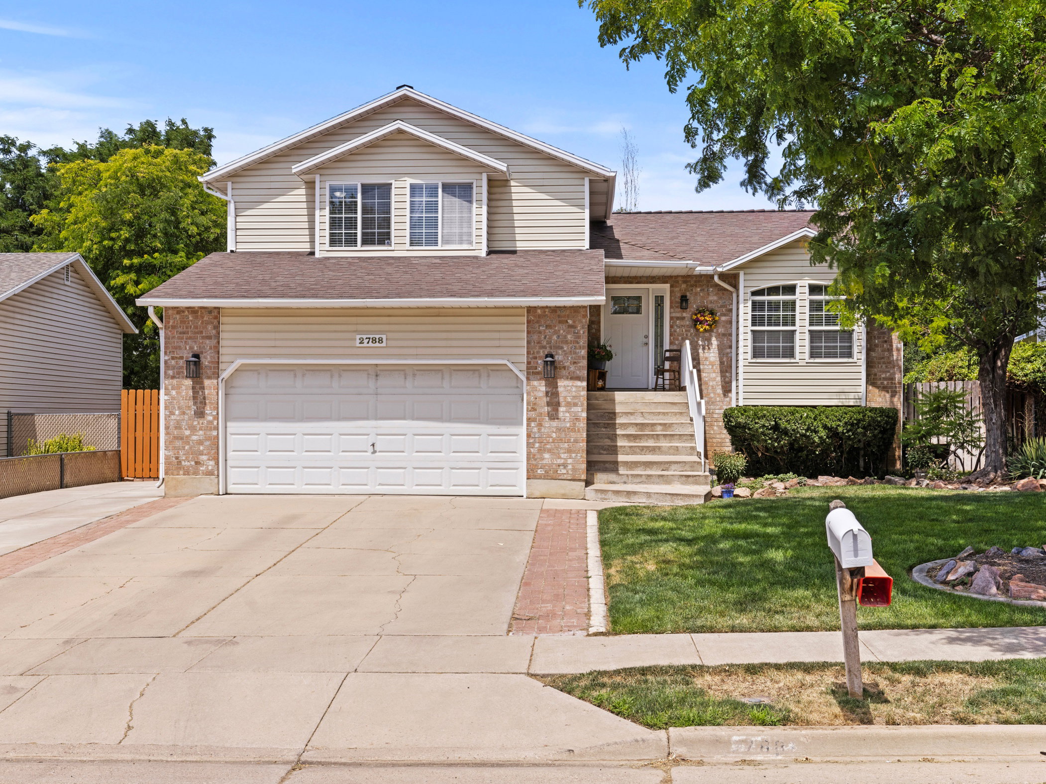 Cream siding exterior with brick accents, featuring an attached two-car garage, concrete driveway, and front entry with steps