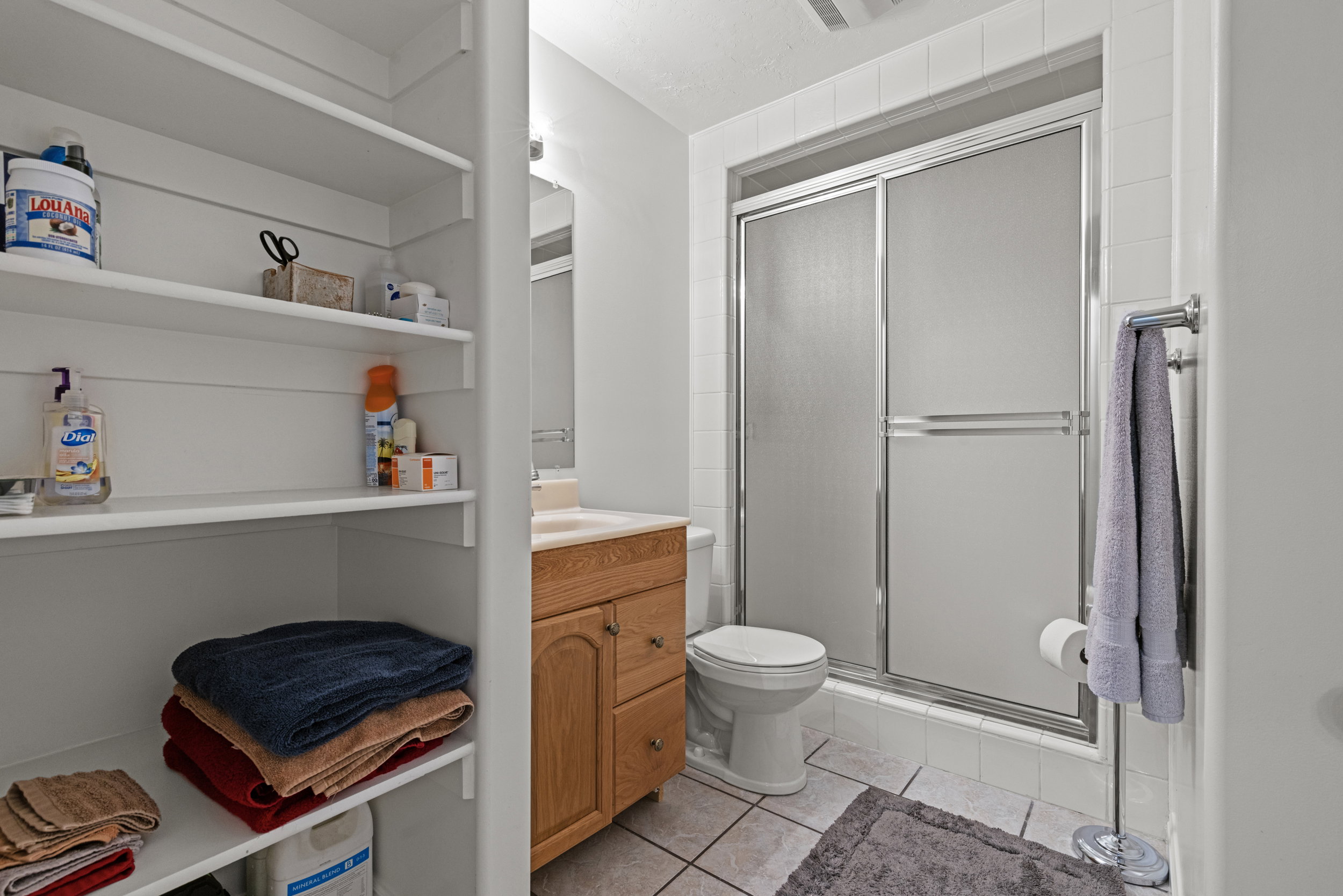 Full bathroom featuring a shower with sliding glass doors, a vanity with a light wood-finish cabinet, and white tile flooring