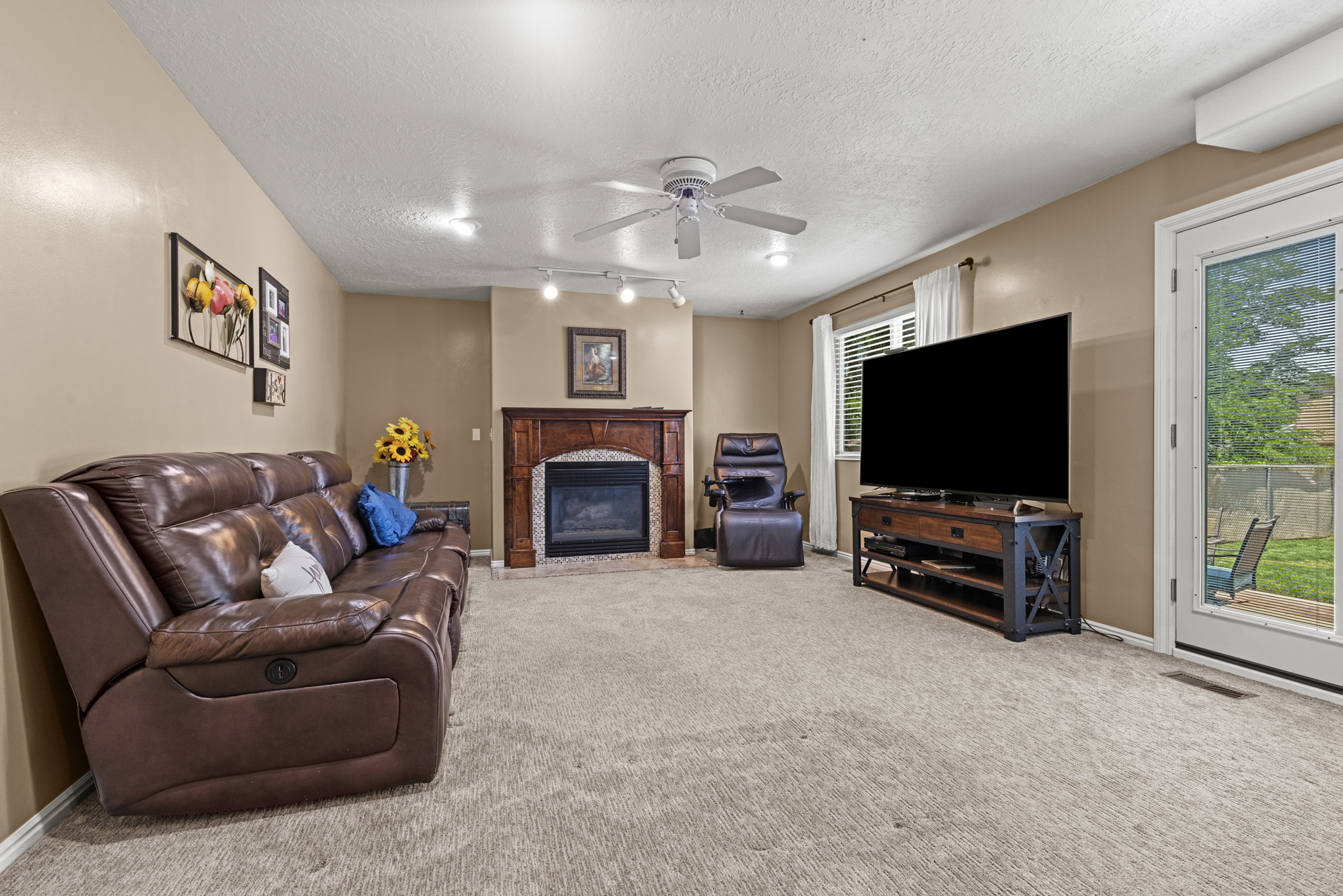 Living area featuring a fireplace with a wood mantle, neutral carpeting, and a ceiling fan with integrated lighting