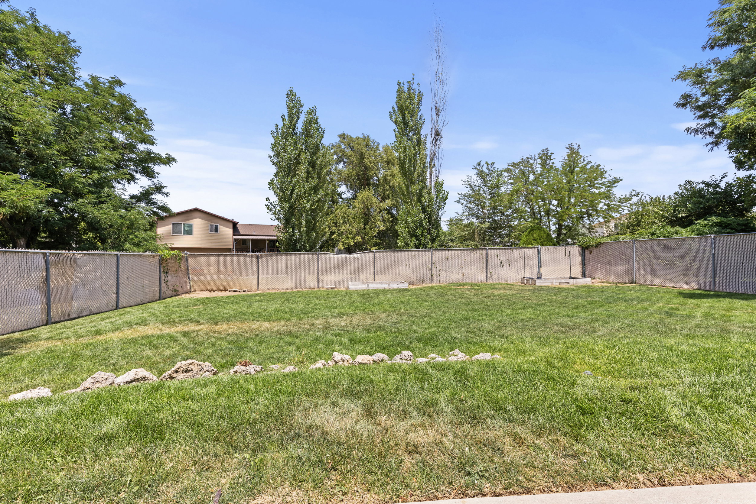 Expansive grassy lawn with surrounding chain-link fencing, mature trees, and a clear sky