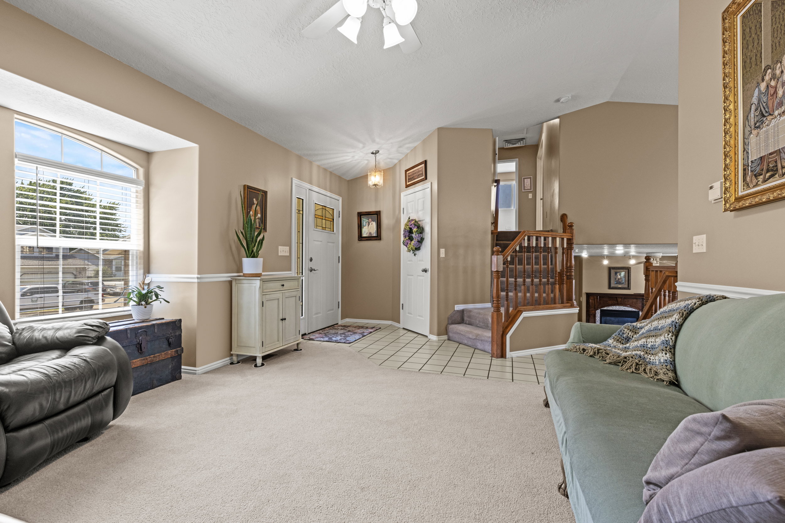 Inviting living area featuring vaulted ceilings, a large arched window with blinds, and light-toned carpet flooring