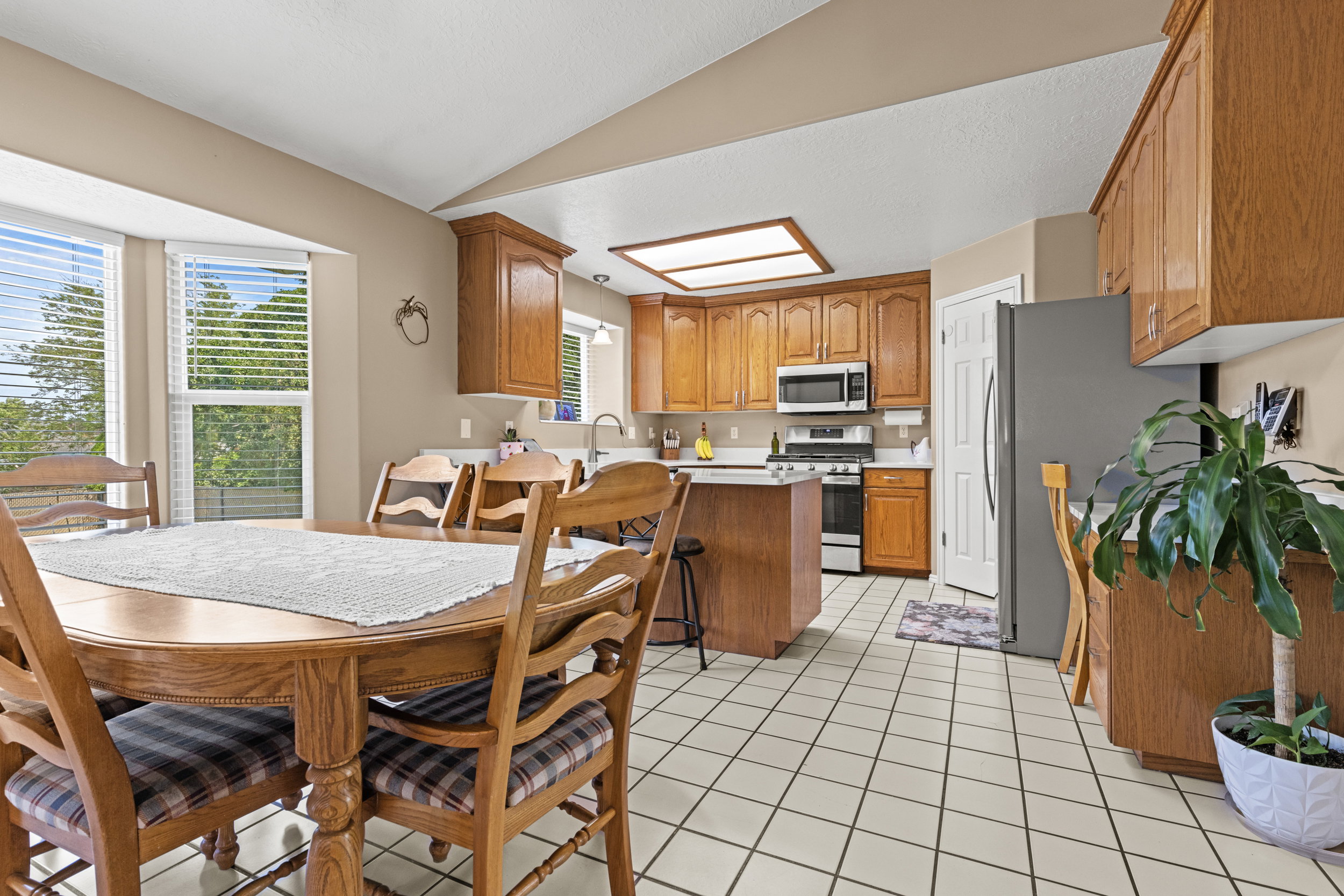 Kitchen and dining area featuring a bay window, wood cabinetry, white tile flooring, and stainless steel appliances