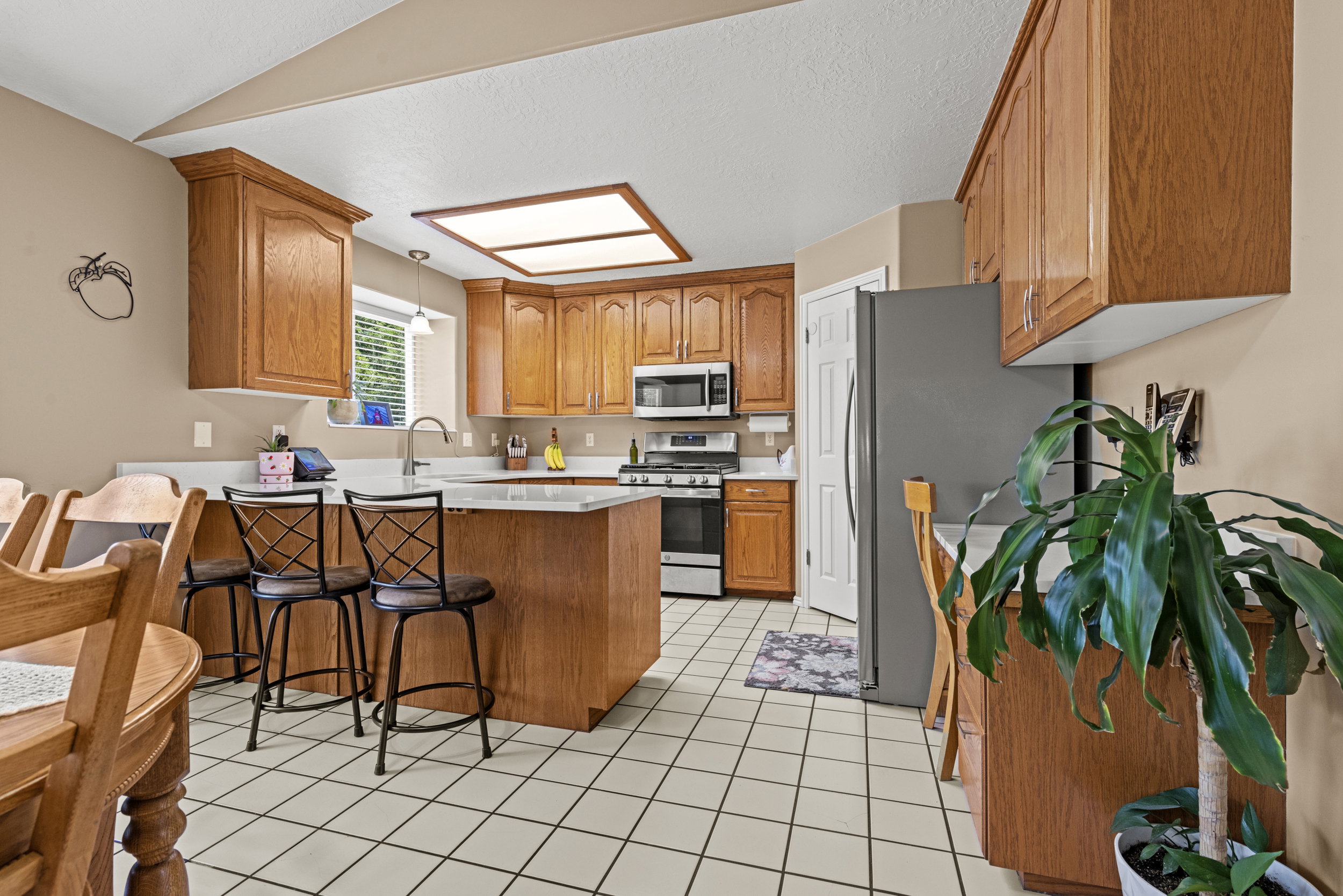 Kitchen featuring wood cabinetry, white countertops, stainless steel appliances, a center island with seating, and white square tile flooring