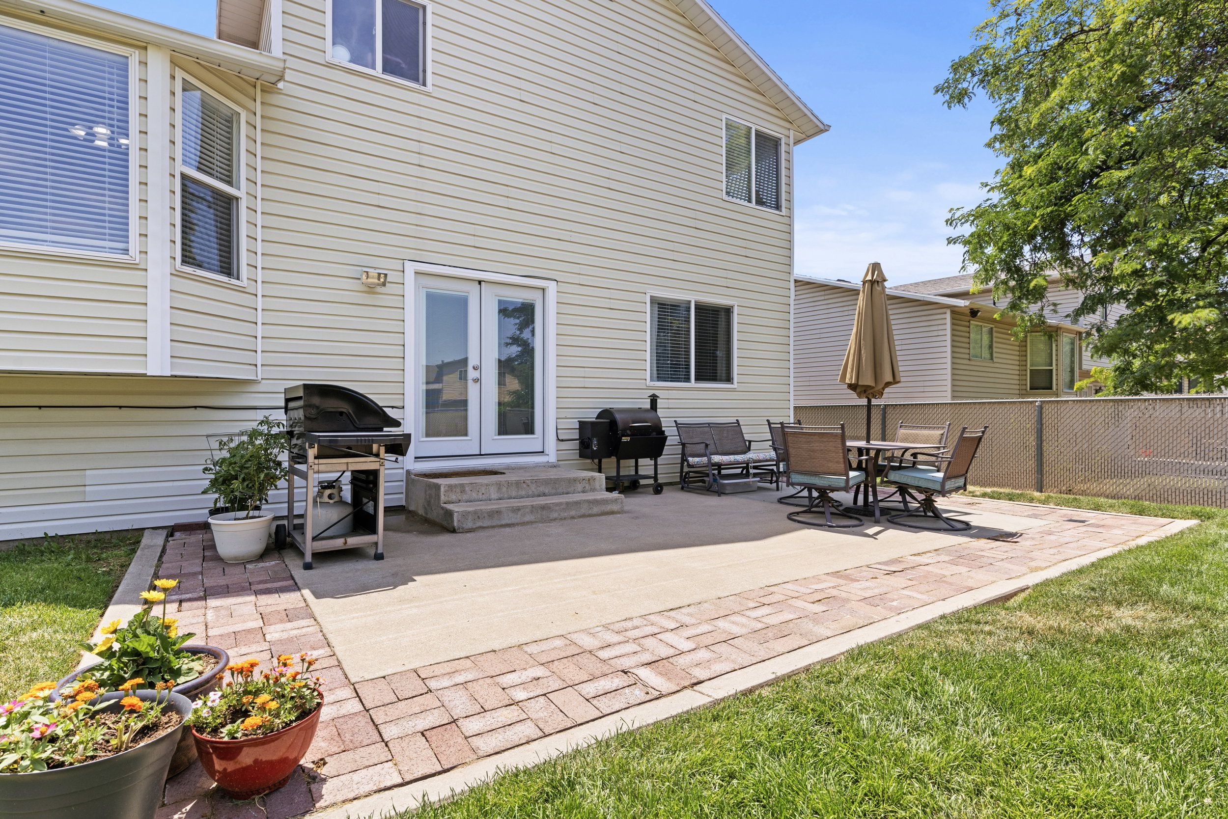 Rear exterior featuring light-toned siding, a multi-level concrete patio with brick paver accents, and a manicured lawn
