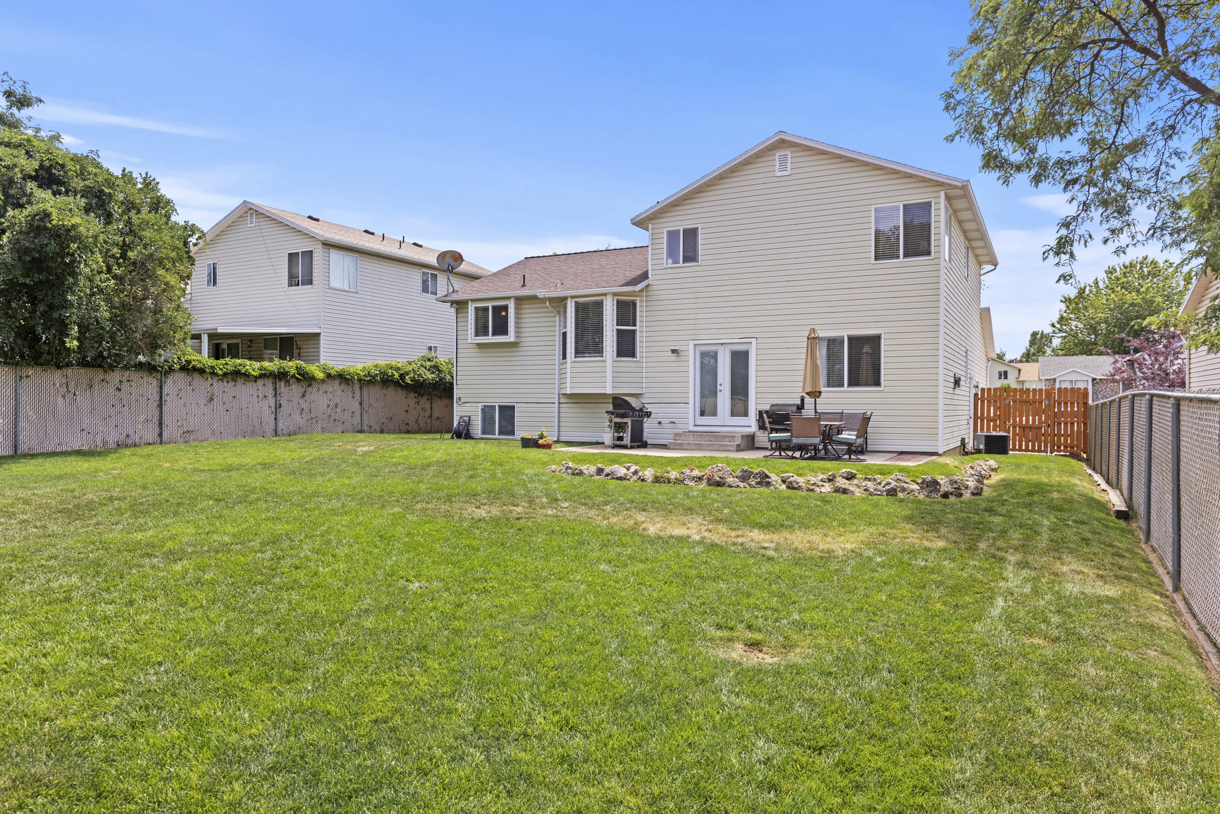 Expansive grassy backyard featuring a paved patio, double white doors, and multiple windows