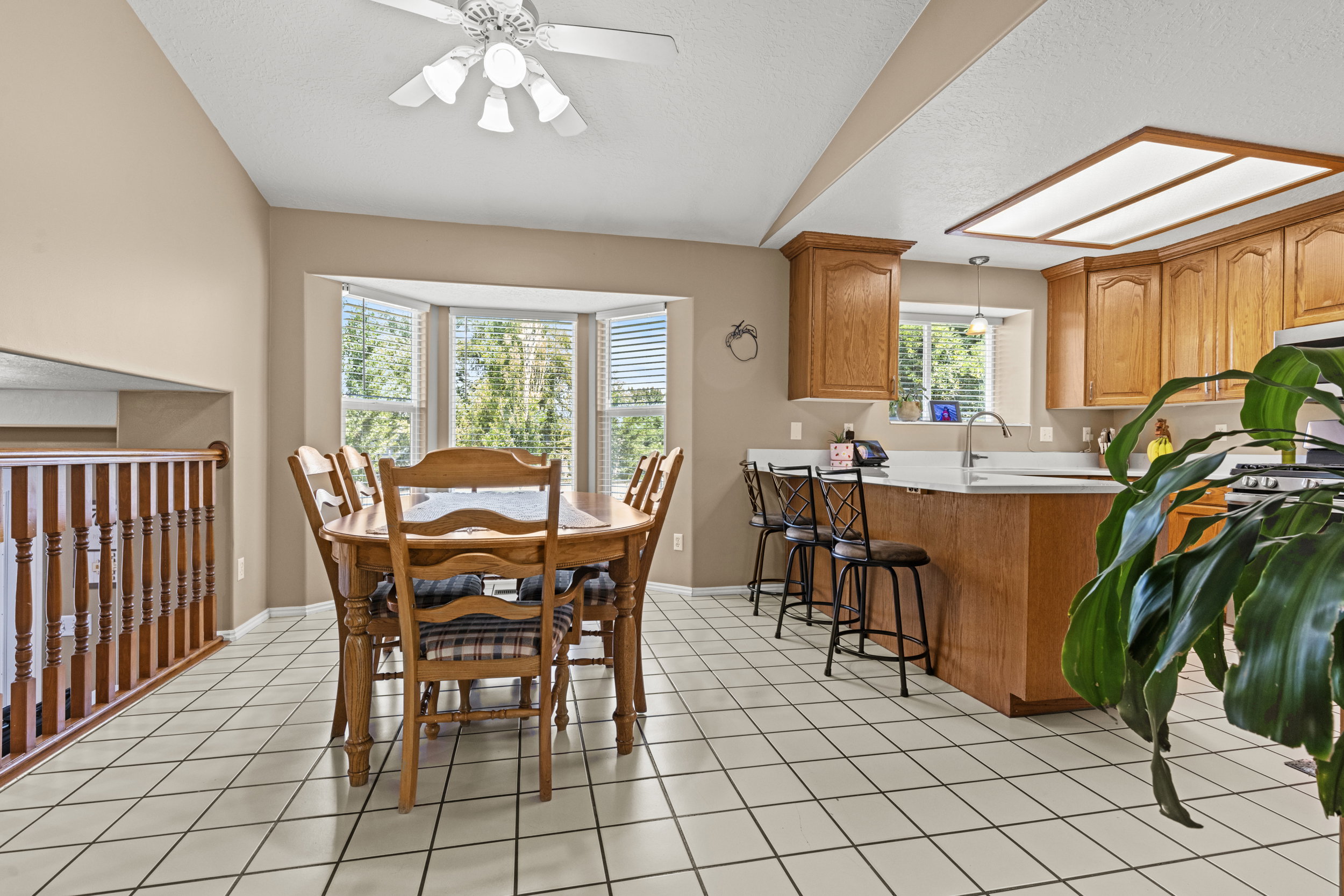 Kitchen and dining area featuring tile flooring, wood cabinetry, a built-in island with seating, a bay window, and a ceiling fan