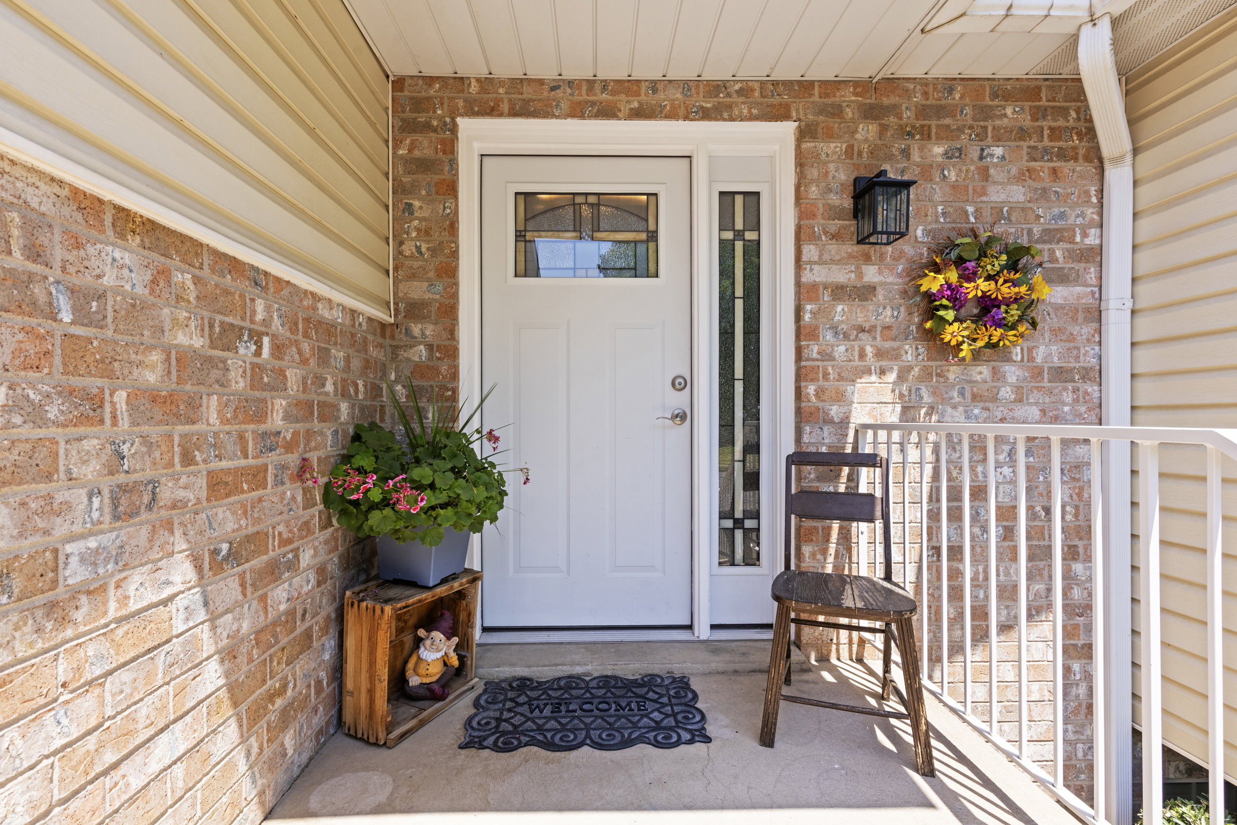 Front entry featuring a white door with decorative glass, a sidelight, brick facade, a concrete porch, and a white railing