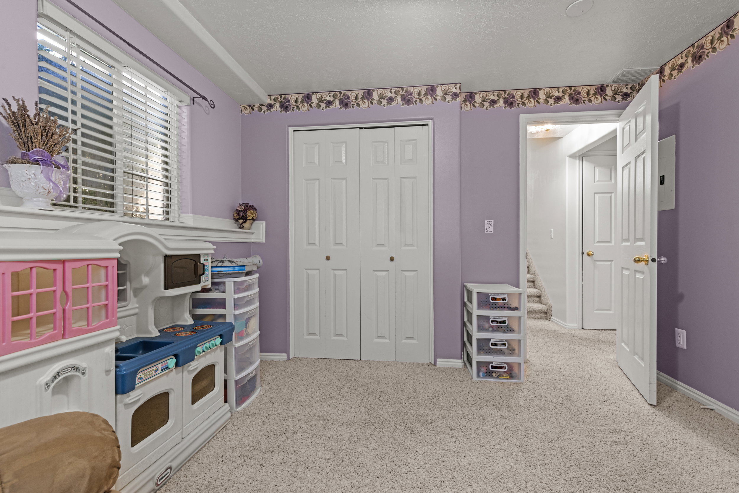 Carpeted room featuring a window with horizontal blinds, bi-fold closet doors, a paneled interior door, and a decorative wallpaper border