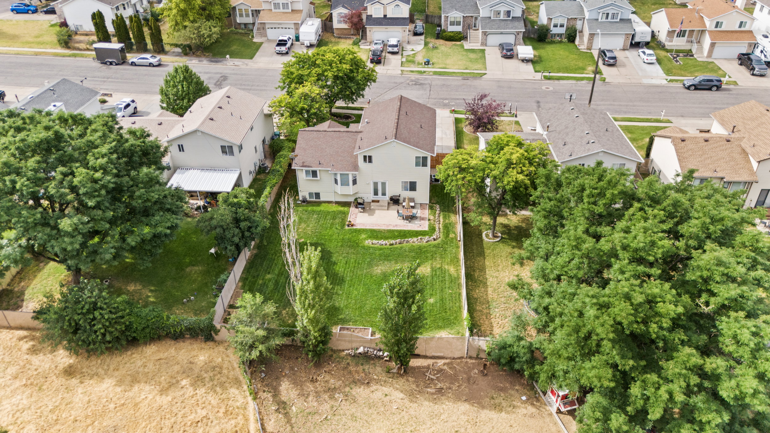 Rear exterior featuring an expansive green lawn, mature trees, a concrete patio, and a privacy fence