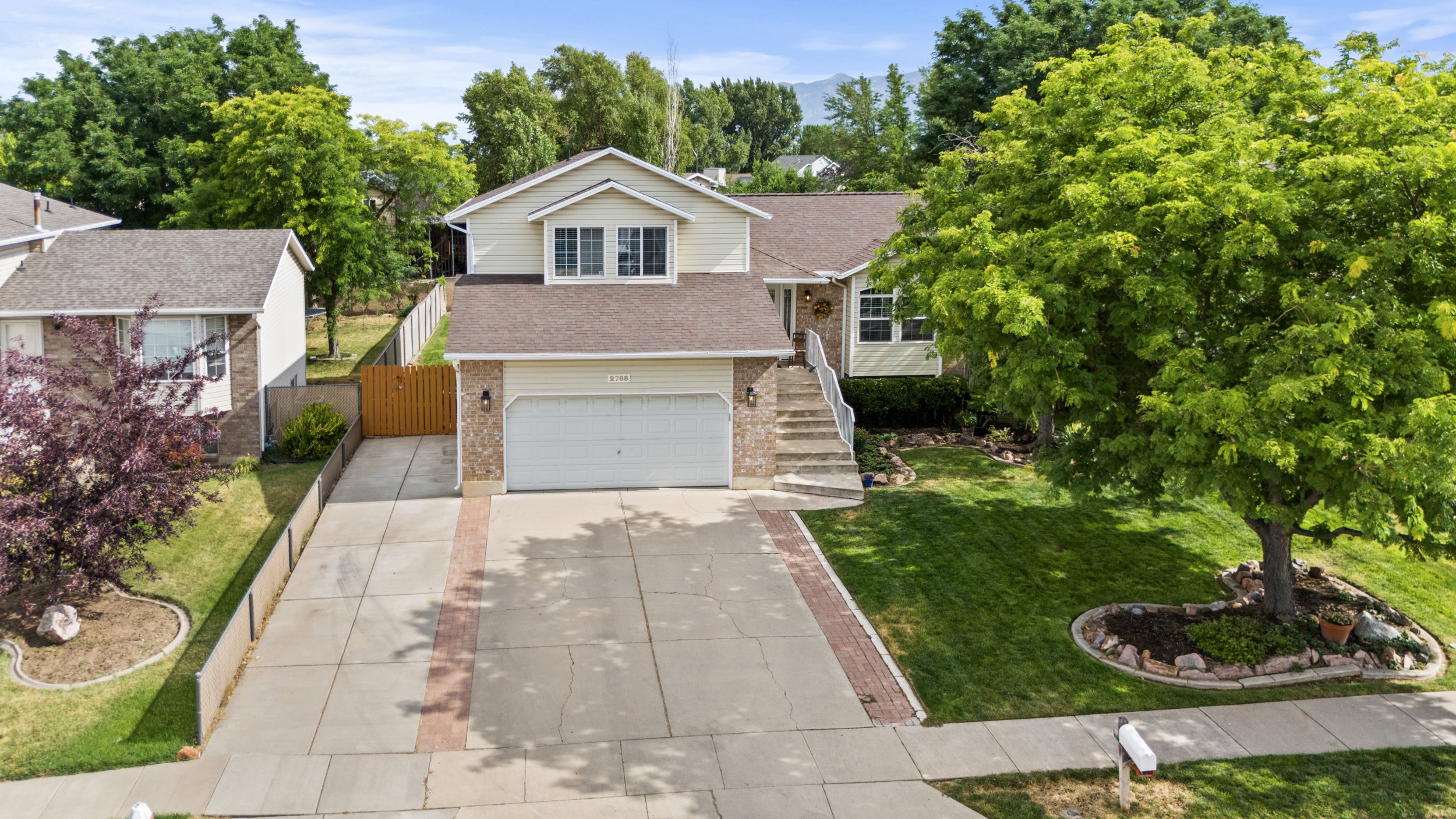 Split-level residence featuring a two-car garage, brick and siding exterior, and a concrete driveway with a brick inlay