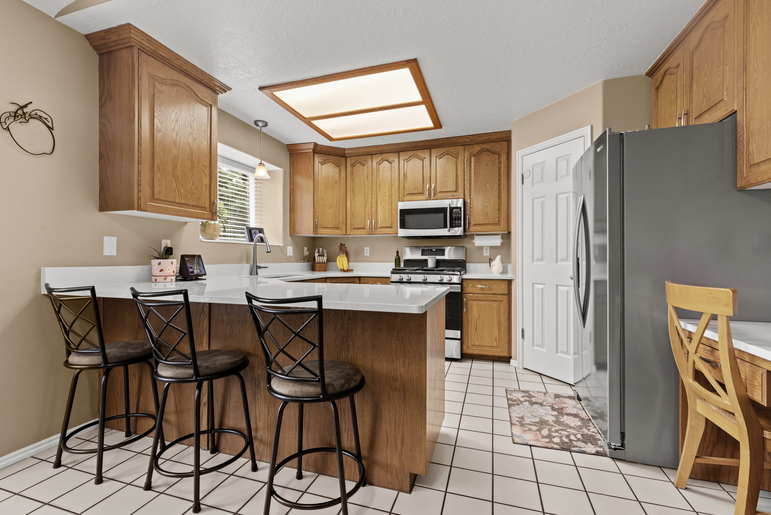 Kitchen featuring wood cabinetry, white countertops, tile flooring, stainless steel appliances, and a central island with bar seating