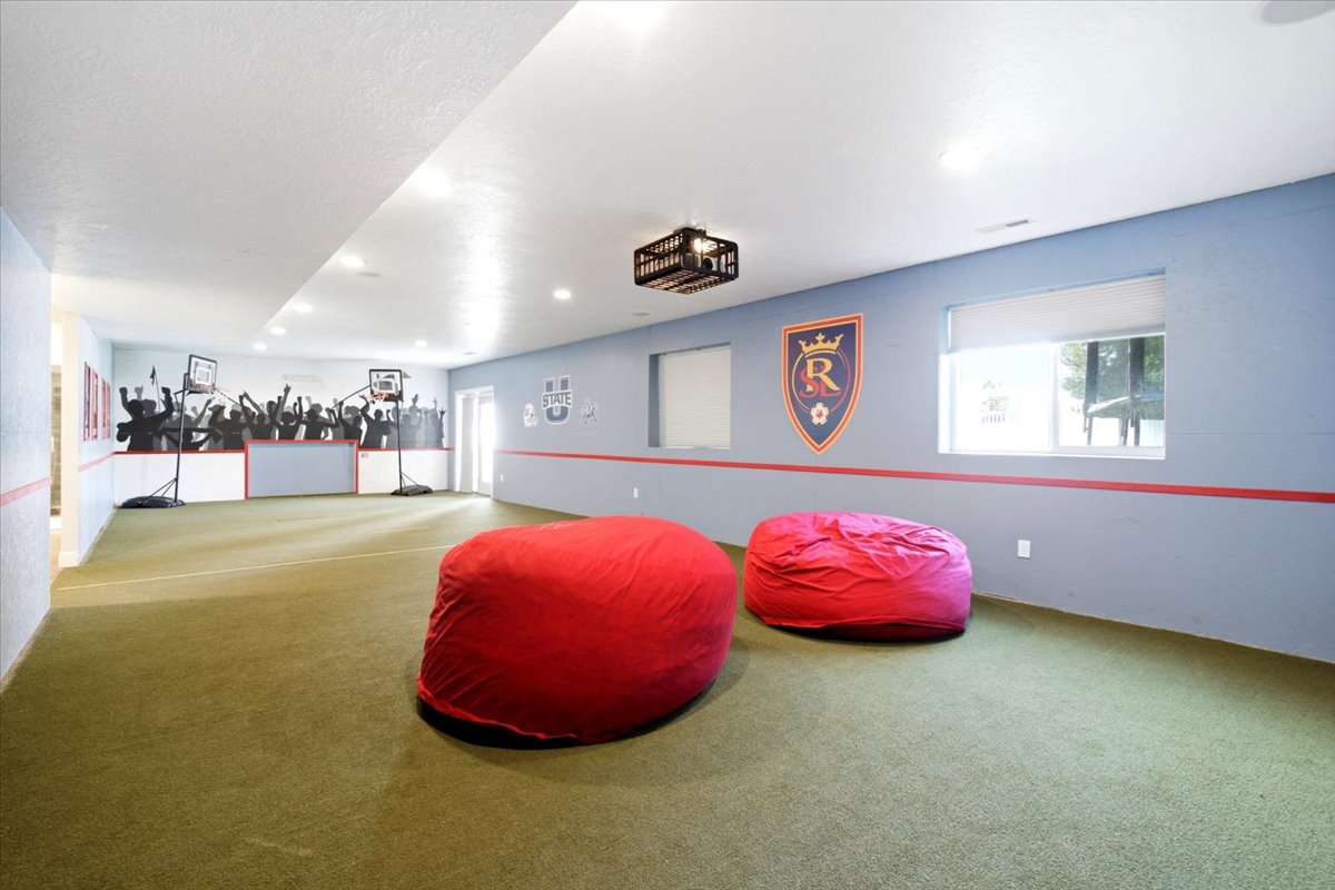 Spacious recreation room featuring light blue walls with a red accent stripe, recessed lighting, and a window with a white roller shade
