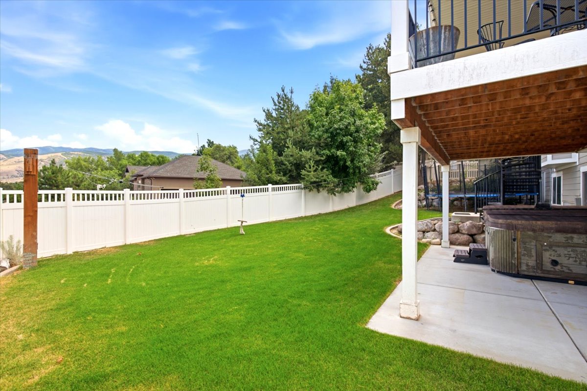 Expansive lawn area featuring a white privacy fence, mature trees, and a concrete patio