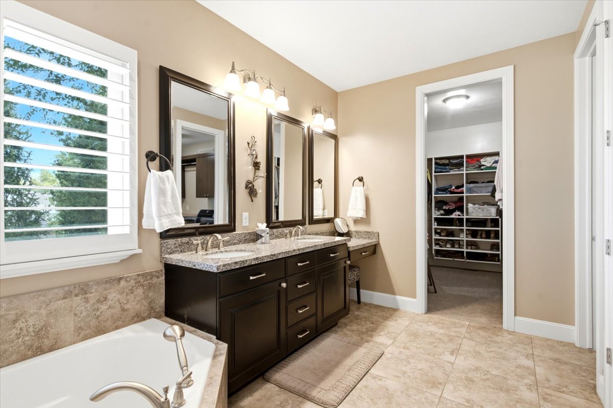 Bathroom featuring a double vanity with dark wood cabinetry, granite countertops, and individual framed mirrors, a large soaker tub, and a separate walk-in shower