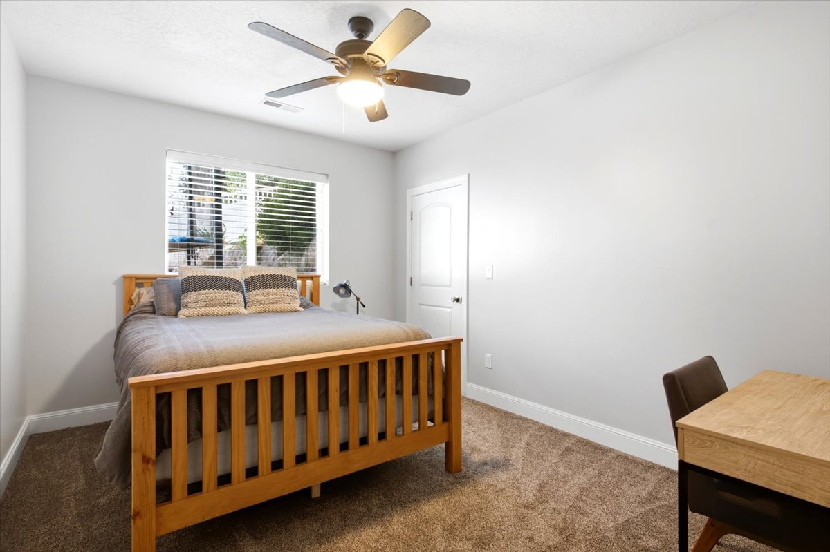 Bedroom featuring light gray walls, brown carpet, a window with horizontal blinds, a white door, and a ceiling fan with integrated lighting