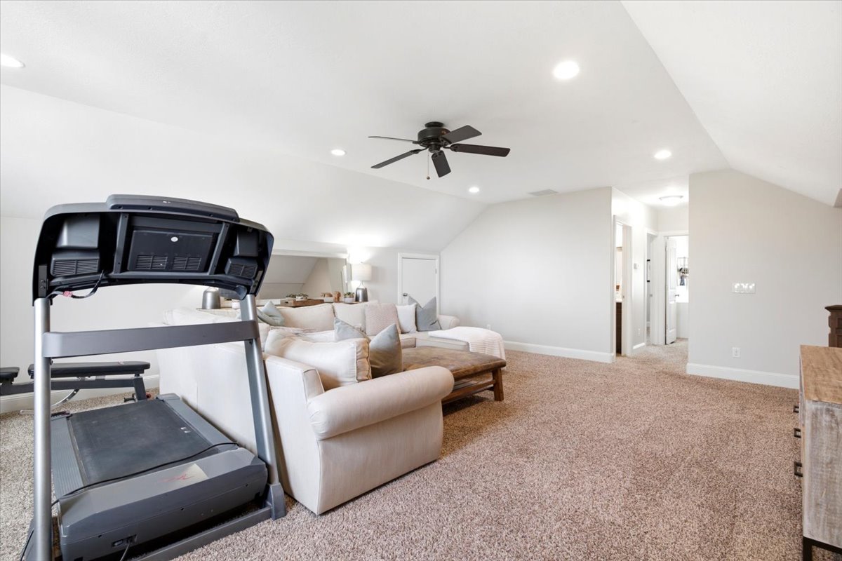 Spacious upper-level room featuring angled ceilings, recessed lighting, and a ceiling fan