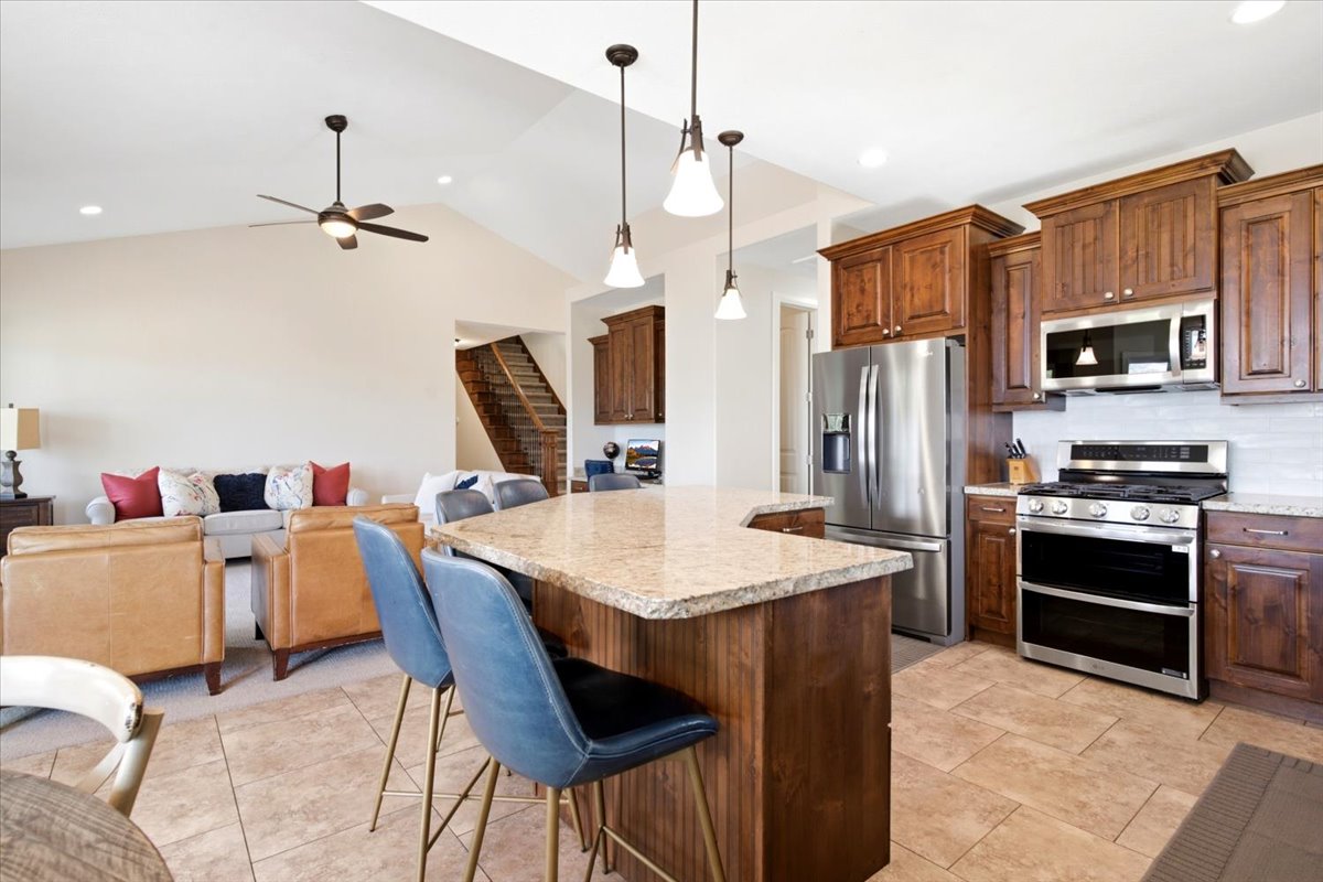 Open-concept kitchen featuring granite countertops, stainless steel appliances, wood cabinetry, and pendant lighting