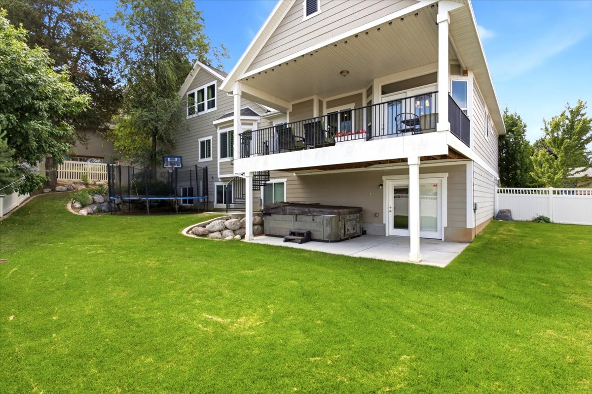 Expansive green lawn surrounds the property, featuring a ground-level patio and a covered upper-level balcony