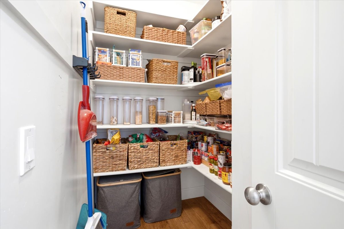 Extra-large walk-in pantry featuring white shelving, wood-finish flooring, and ample storage space