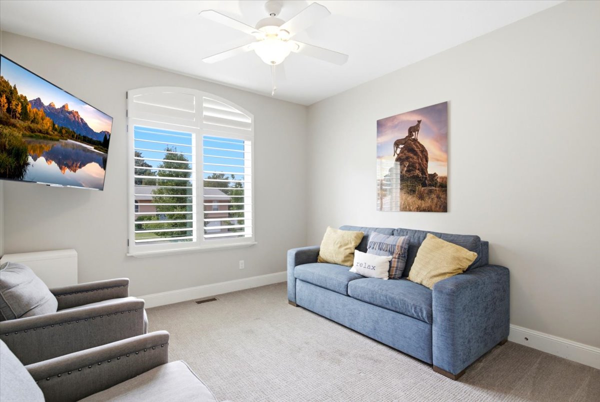 Carpeted room featuring a ceiling fan with integrated lighting, a wall-mounted television, and a window with custom arched plantation shutters