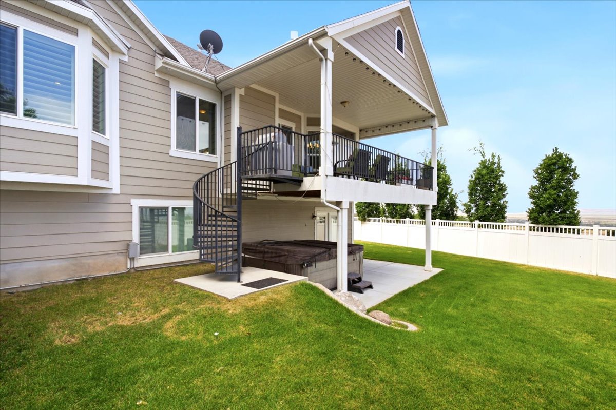 Rear exterior featuring a covered deck with black railing, a spiral staircase, a lower-level patio, and a white privacy fence