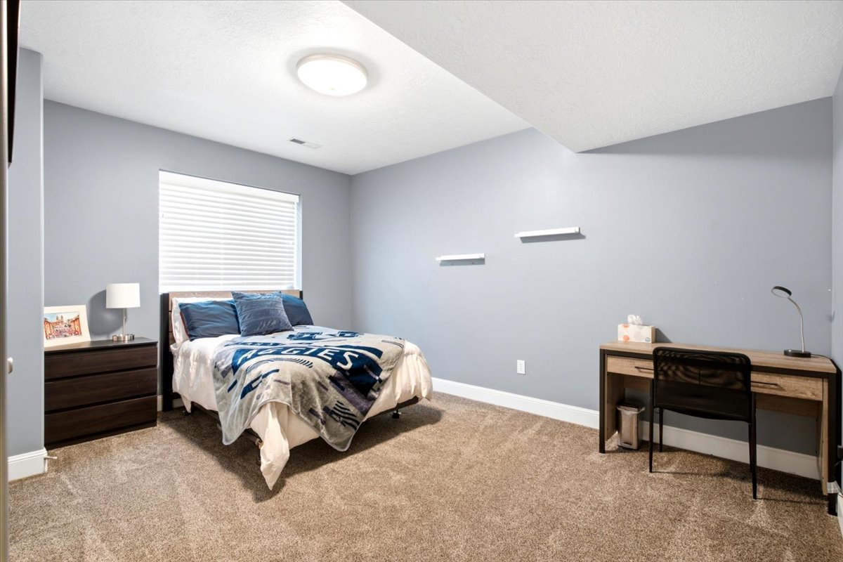 Bedroom featuring light blue walls, a rectangular window with blinds, and neutral-toned carpeting