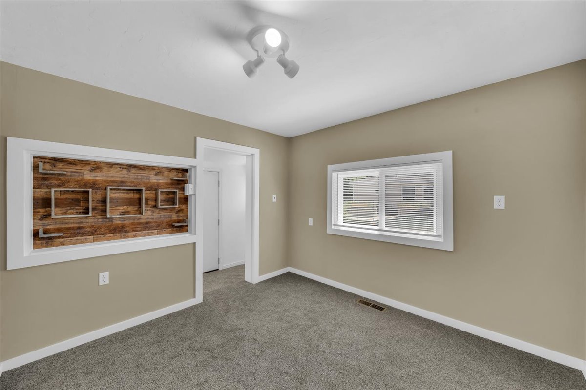 Built-in wood-finish wall feature with floating shelves, neutral wall paint, white trim, track lighting, and gray carpeting