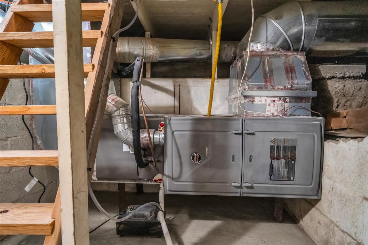 Utility area featuring a forced-air furnace with visible ductwork and a nearby wooden staircase