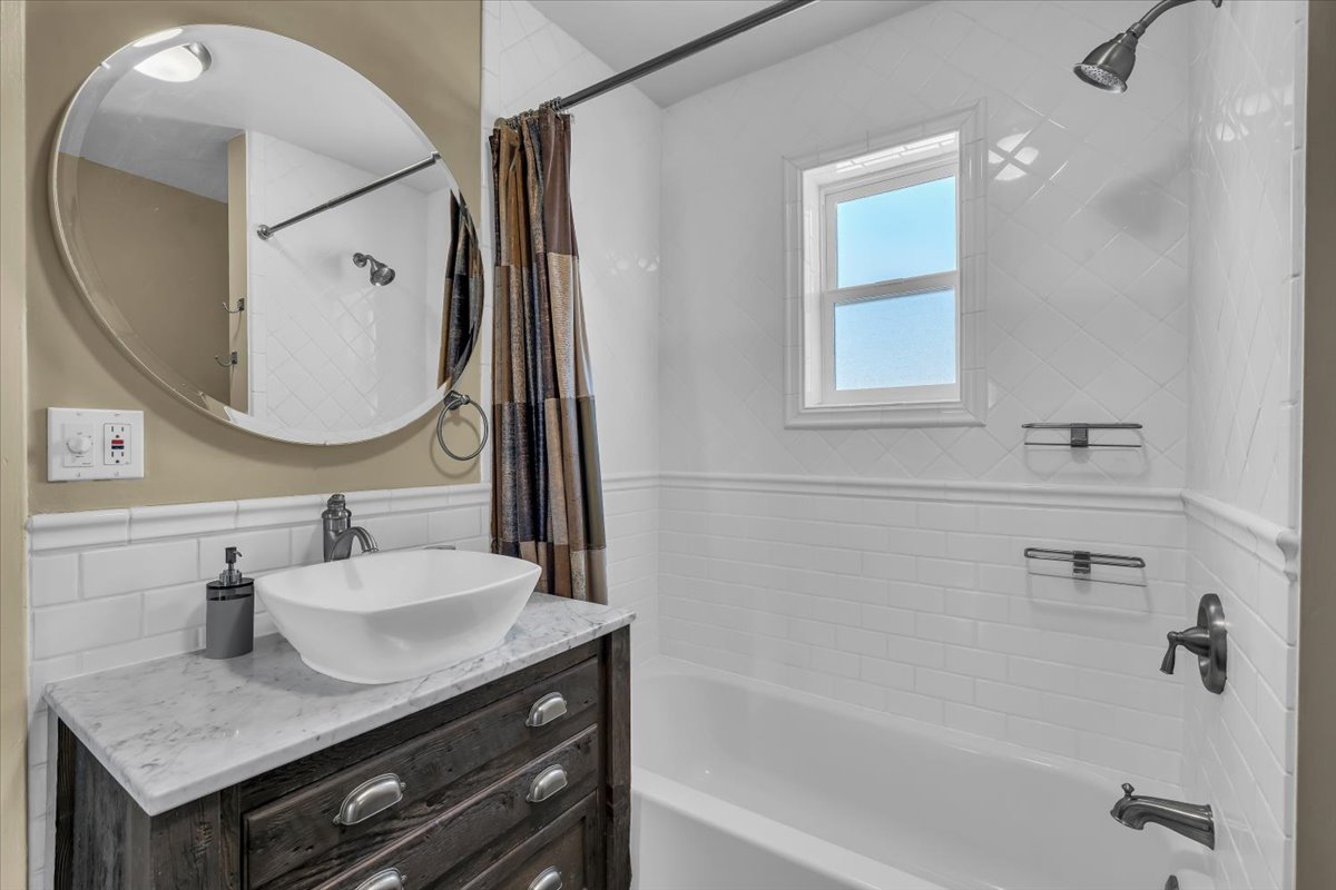 Bathroom featuring a dark wood-finish vanity with a vessel sink, a marble-look countertop, and a round wall-mounted mirror