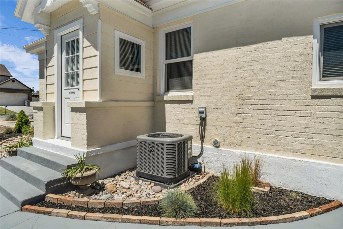 Exterior siding with a windowed entry door, a rock and mulch landscape bed, an exterior wall with brick detailing, and a modern HVAC unit
