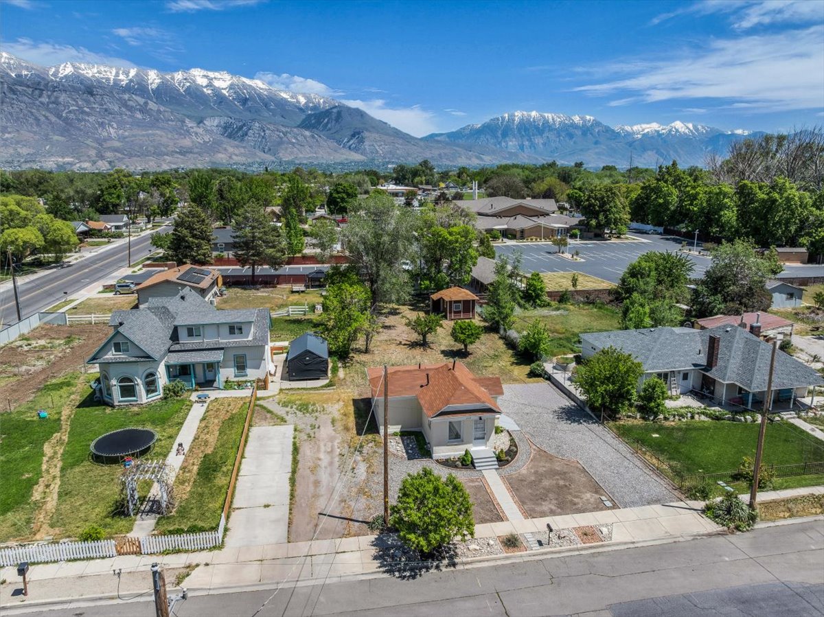Aerial perspective showcasing multiple properties, including a prominent two-story residence with a light-colored exterior and a dark roof, and a single-story home with a red-orange roof