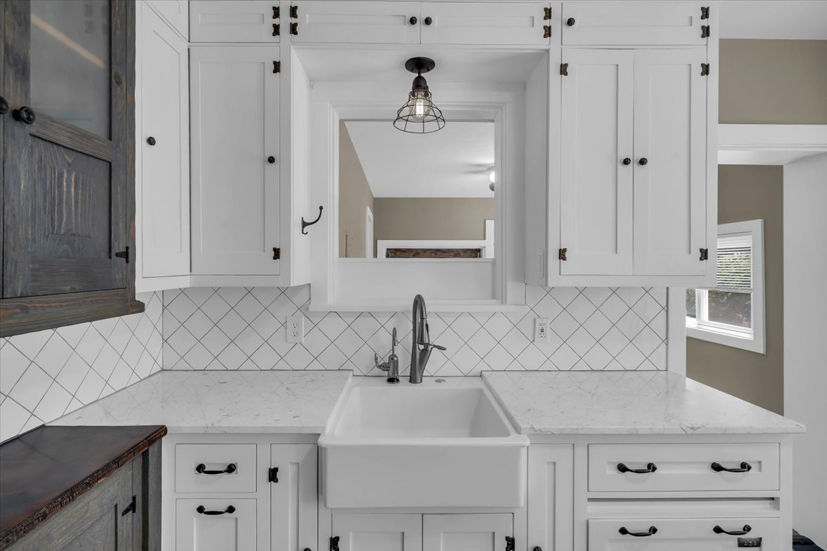 White shaker cabinetry with dark hardware, a farmhouse-style sink, and light-toned countertops