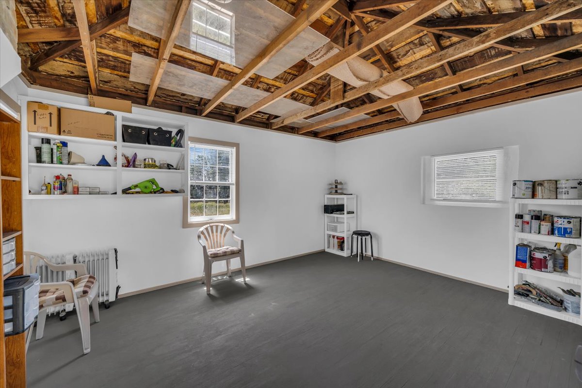 Exposed ceiling joists with unfinished subfloor above, painted concrete flooring, white walls, and multiple built-in shelving units