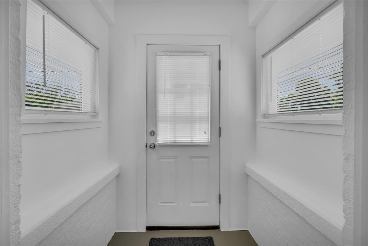 Entryway featuring a white paneled door with an upper window, two side windows with blinds, and white textured low walls